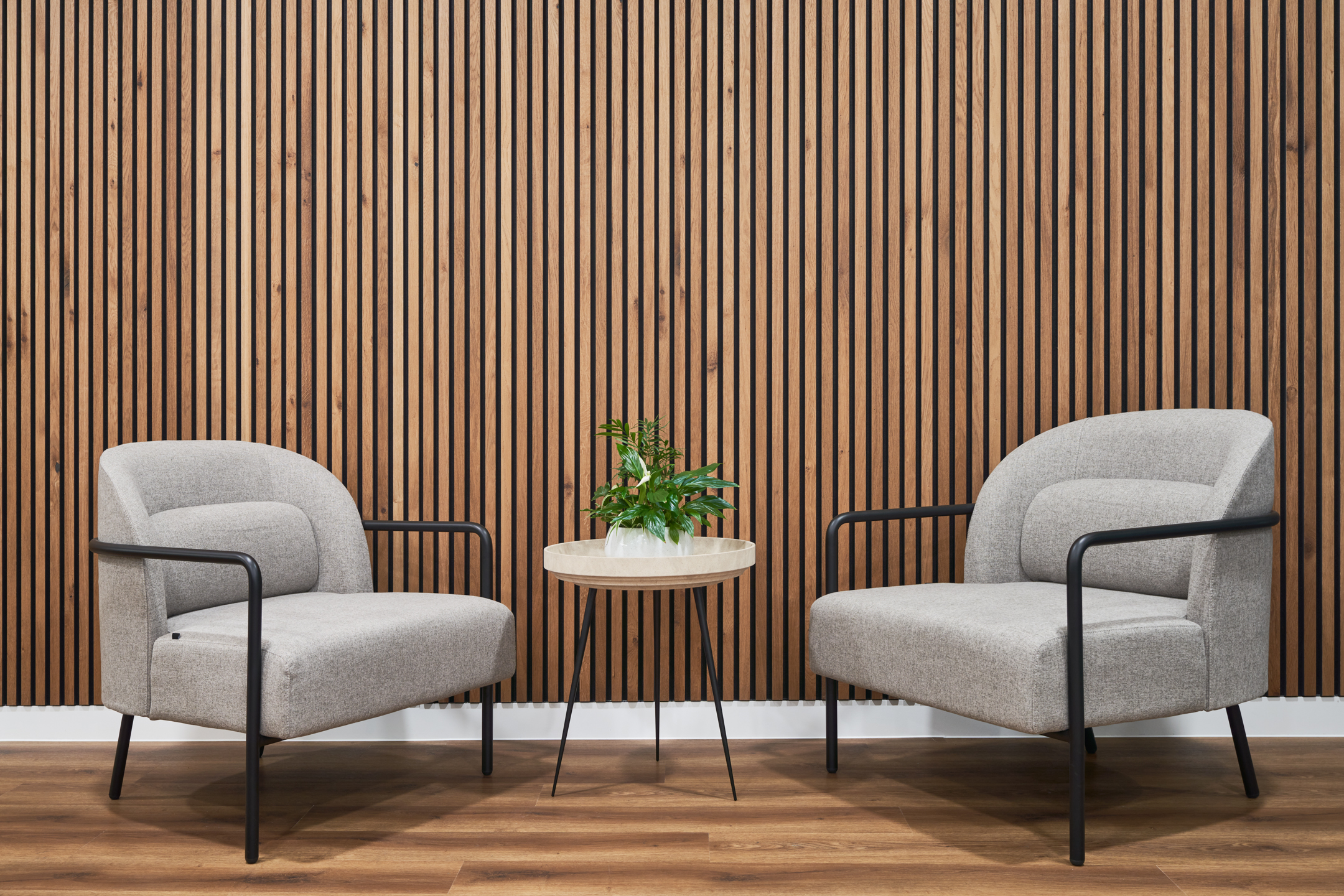 Soft seating supplied to LGC with two grey armchairs and a round table, set against a timber slat wall feature.