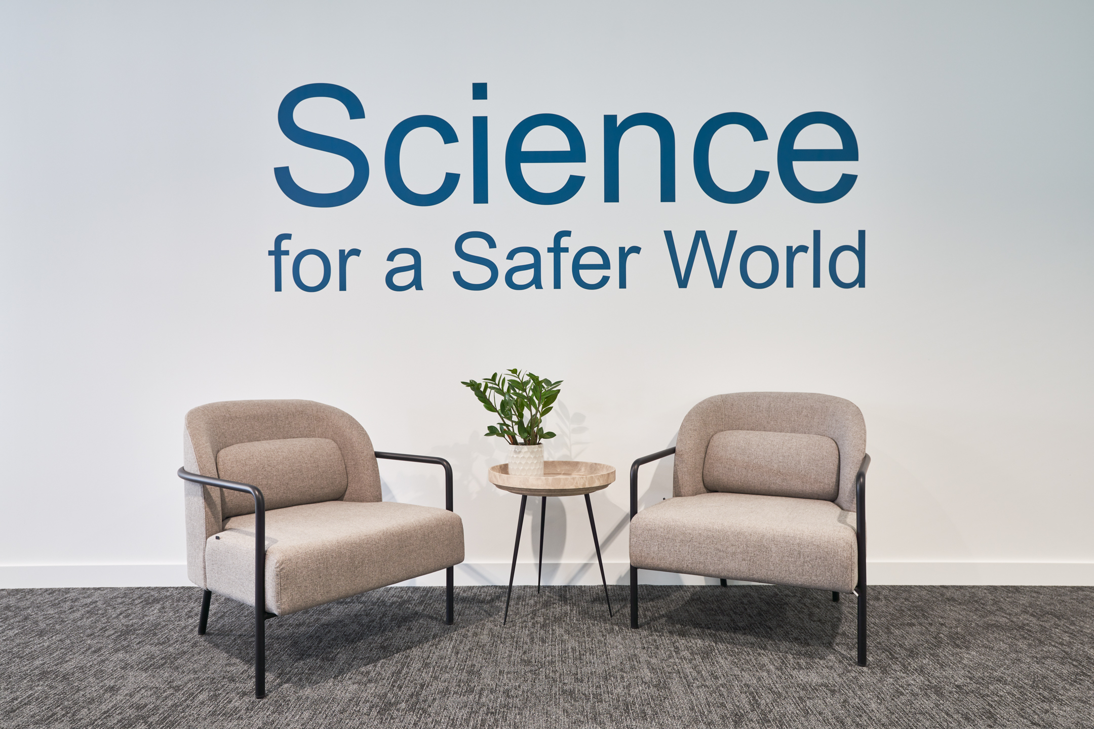Soft seating area at LGC with two armchairs and a round table, positioned beneath the brand message 'Science for a Safer World'.