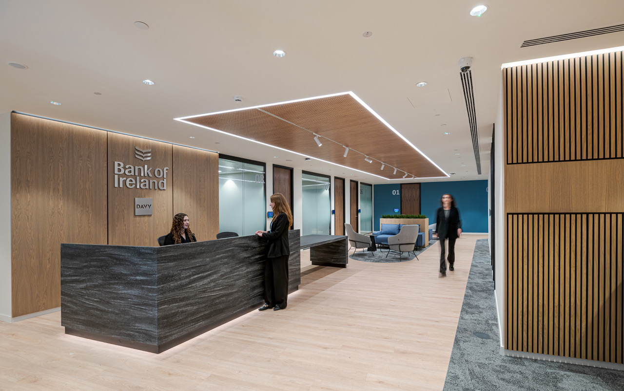 Bank of Ireland reception area with tonal lounge seating and a bold stone desk, reflecting the brand through material choices and formal comfort.