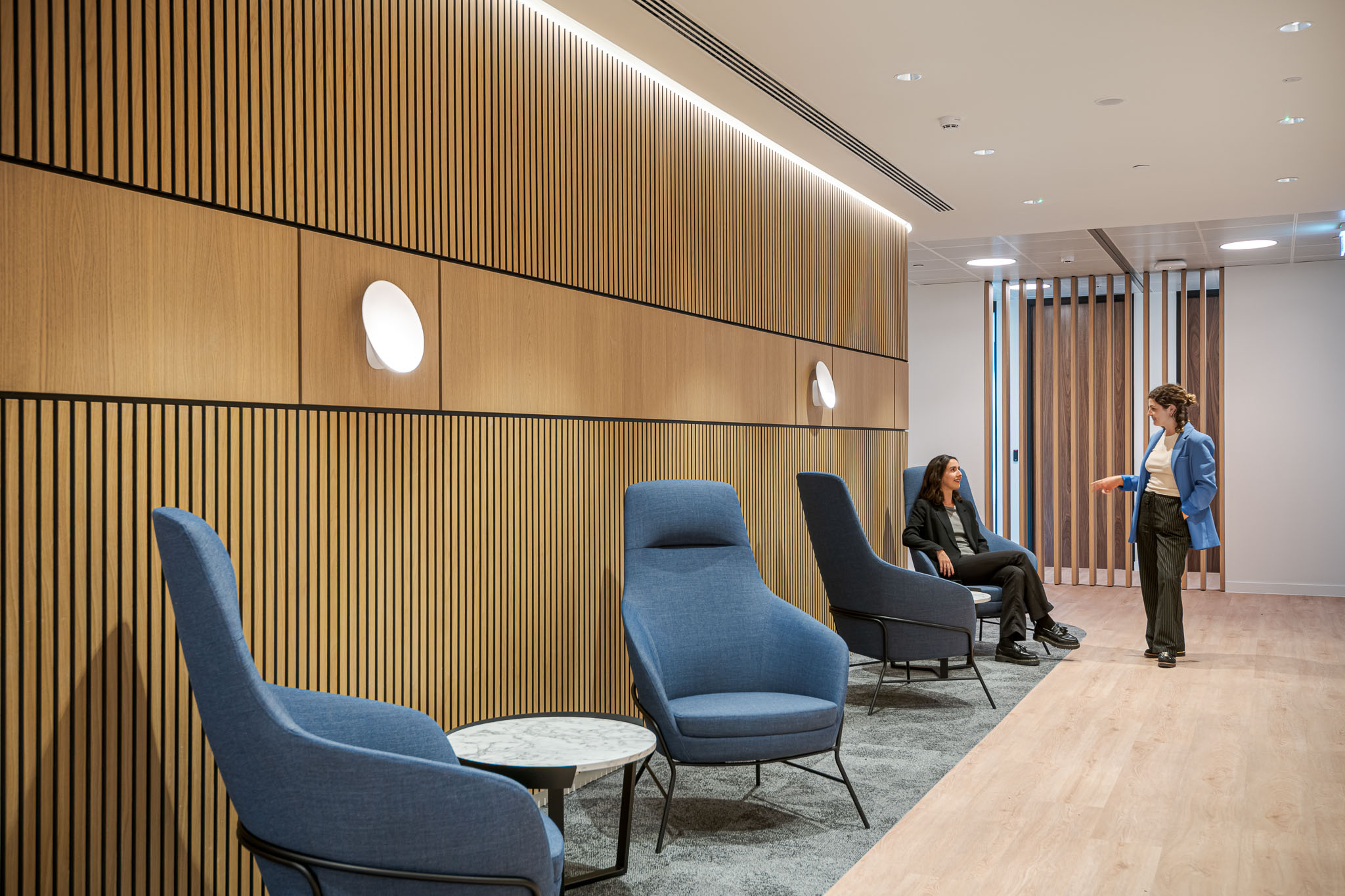 Bank of Ireland client lounge with high-back armchairs in blue fabric, styled to bring comfort and privacy against a warm timber slatted backdrop.