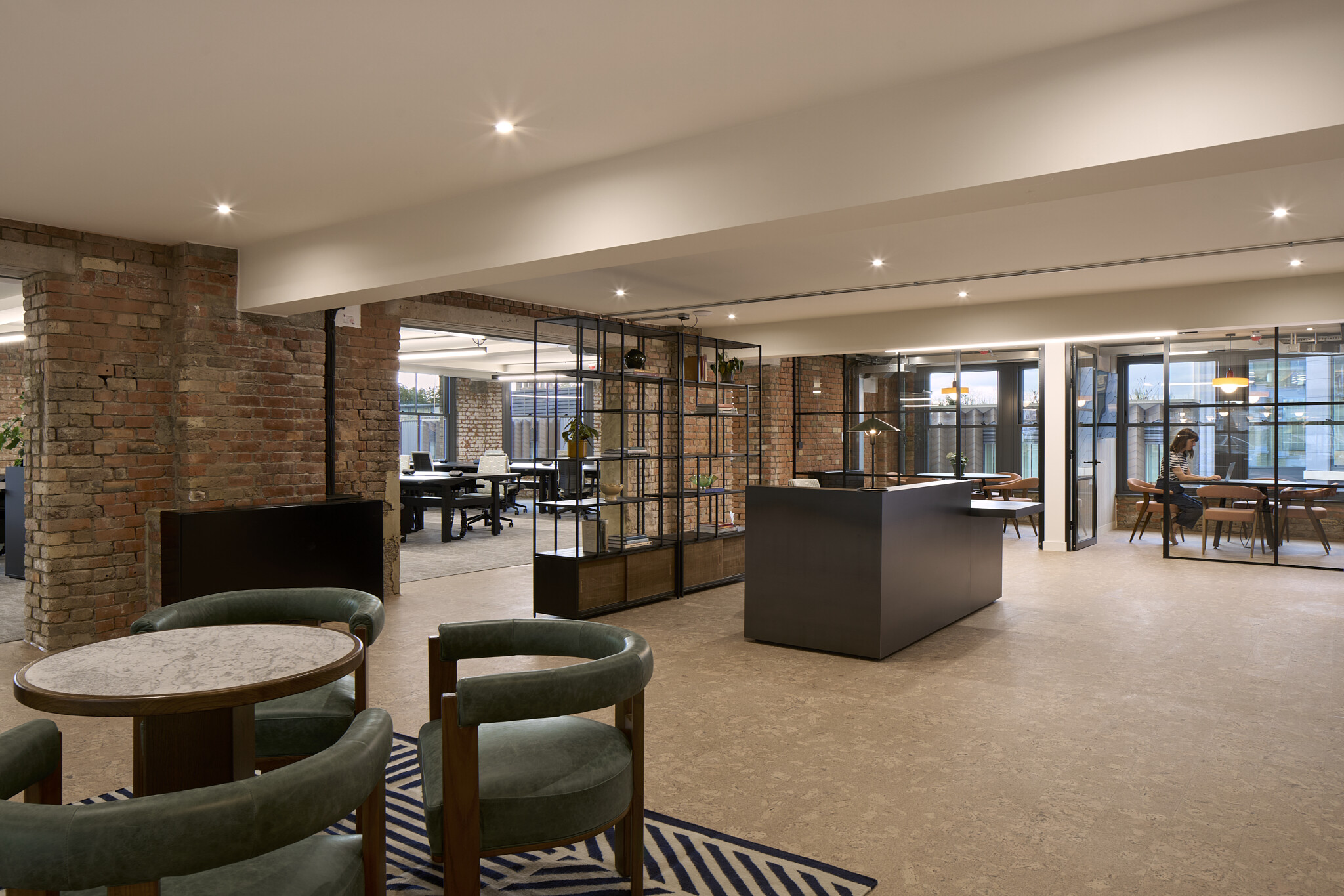 The Waterman reception with marble-topped seating, black desk, open shelving and glazed meeting rooms within an exposed brick interior