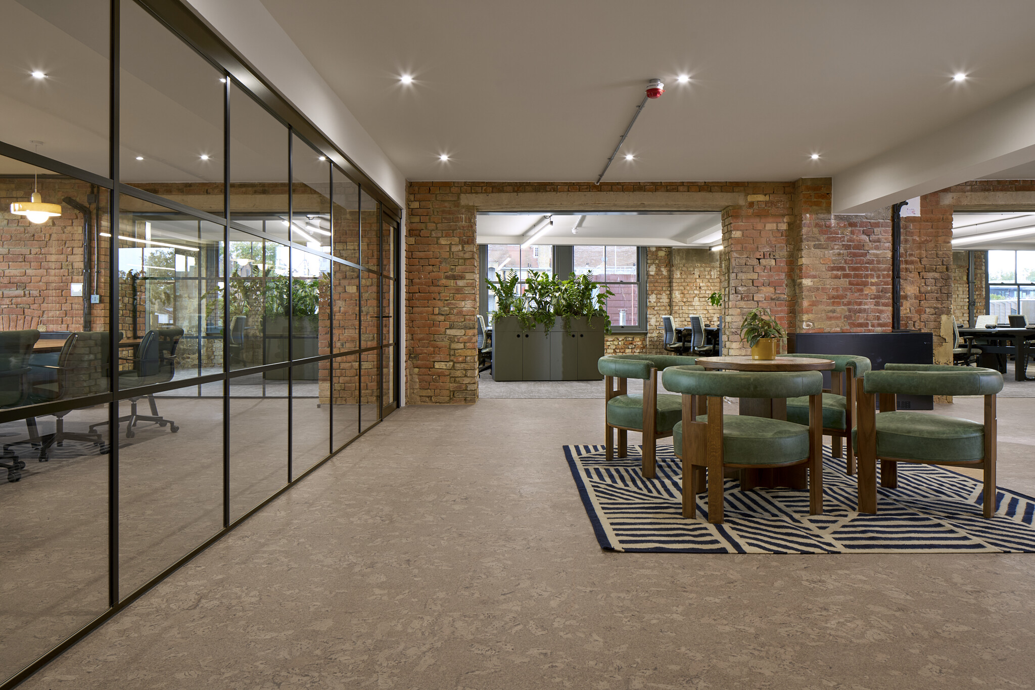 The Waterman workspace with crittall-style glazing, green lounge chairs on a patterned rug and planters zoning the open plan