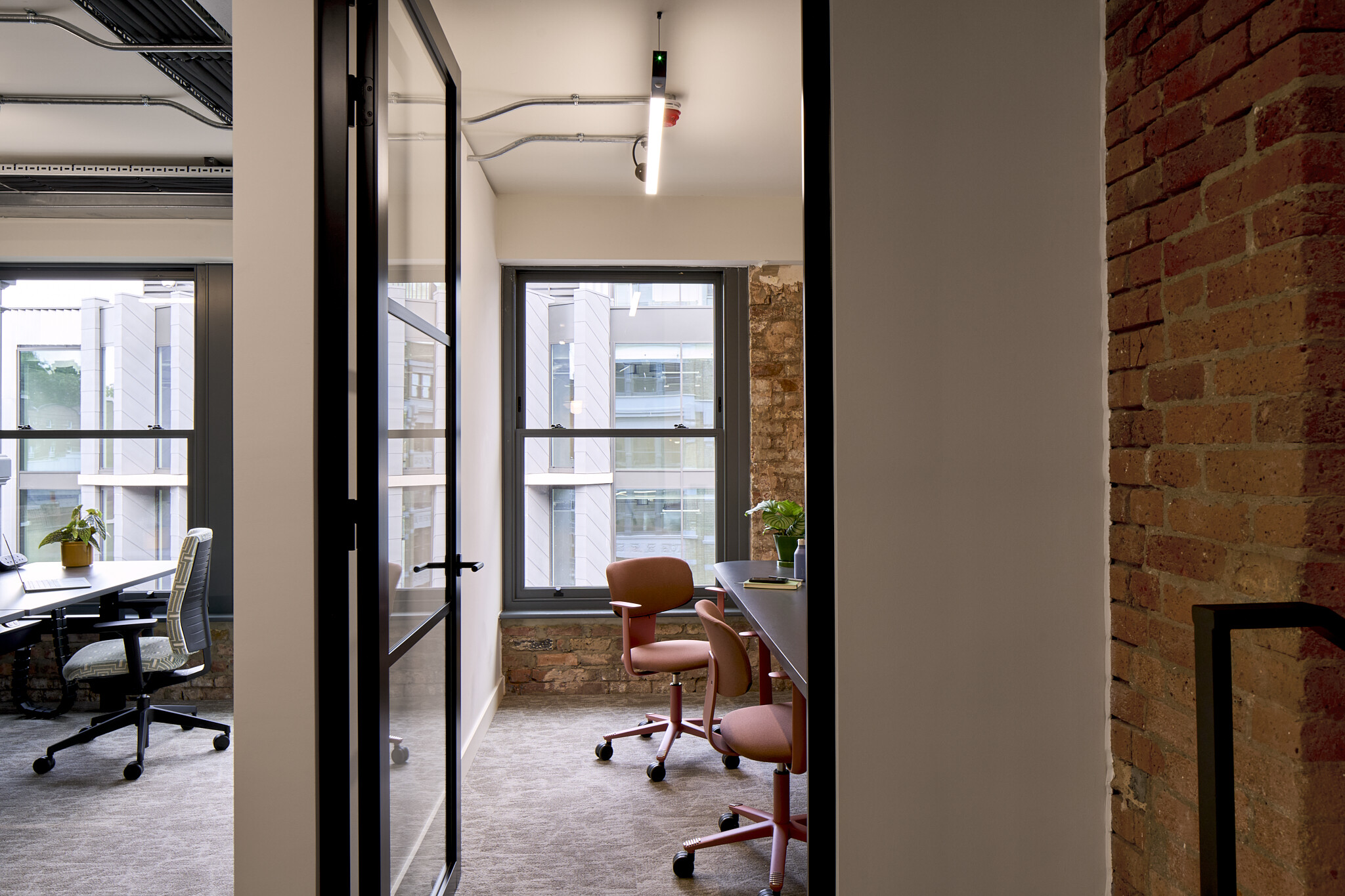 The Waterman focus room with pink task chairs, exposed brickwork and large windows bringing natural light into a quiet meeting space