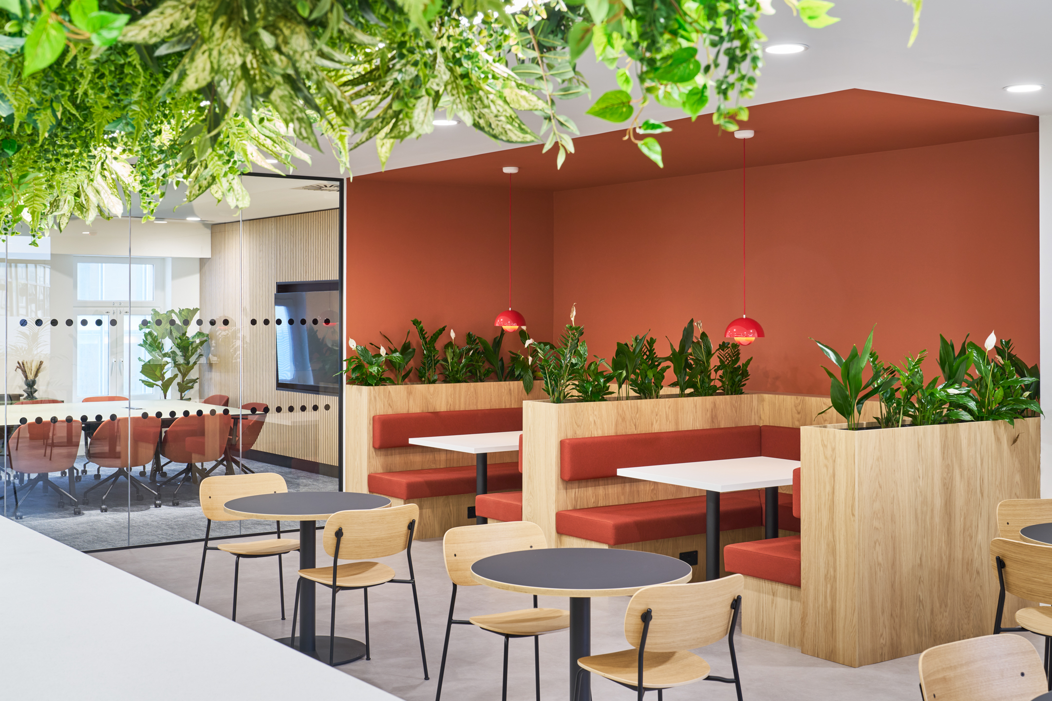 Built-in booths with red accents and planting at 7 Bishopsgate, Level 4, furnished by Platfform for BGO, adjacent to meeting rooms and casual seating areas.