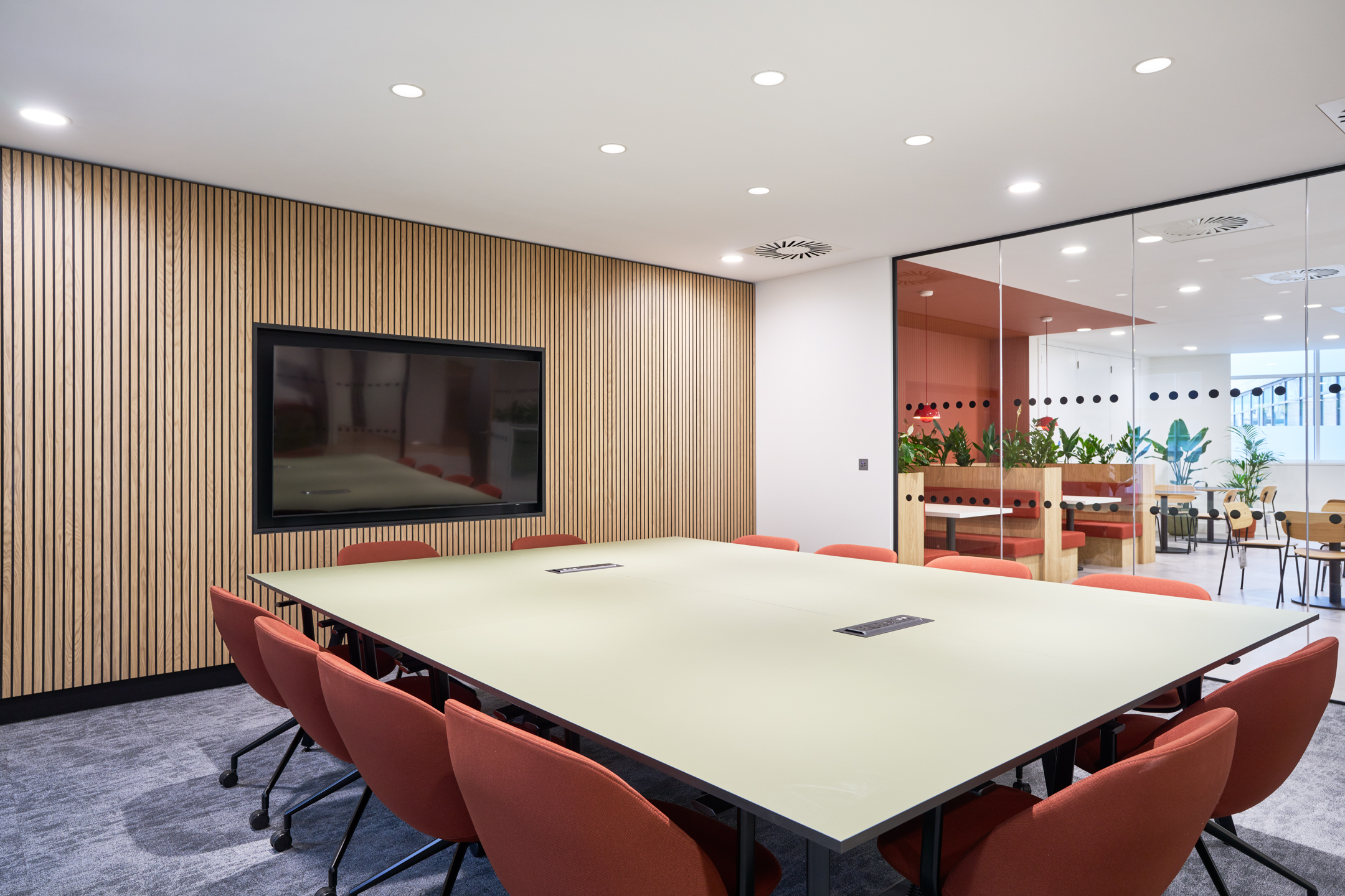 Glass-fronted meeting room at 7 Bishopsgate, Level 4, with integrated AV and bold red chairs, furnished by Platfform for BGO alongside adjacent booth seating.