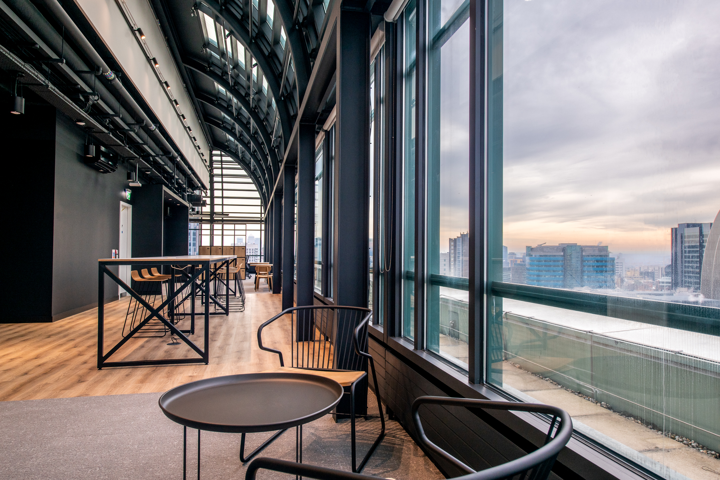 Breakout area at 135 Bishopsgate with skyline views at sunset, furnished by Platfform for British Land with black steel-frame tables and lounge seating.