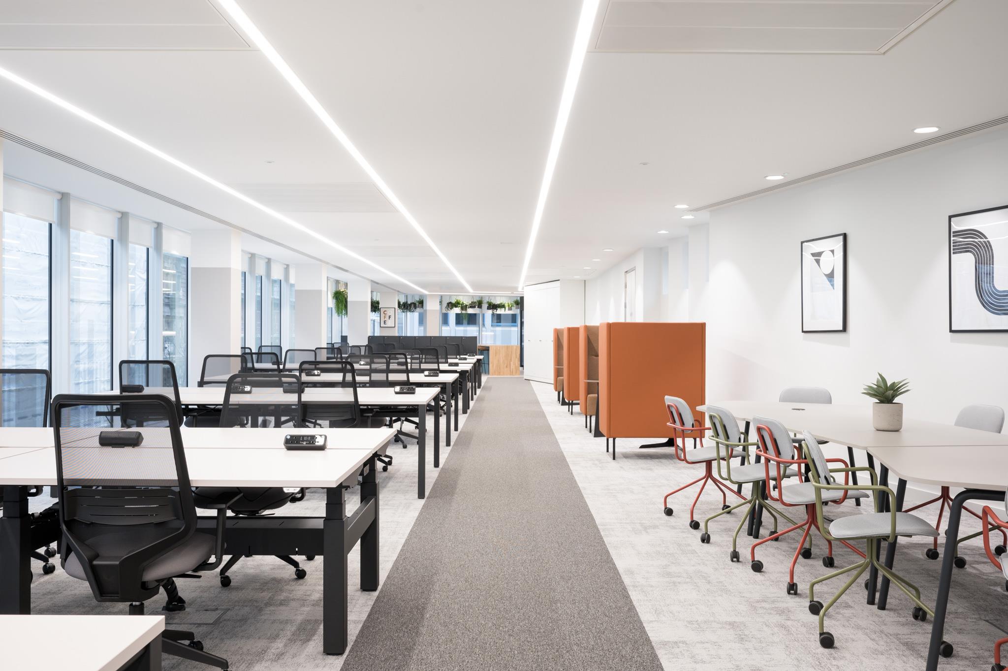 Open-plan workspace at Platfform’s 70 New Oxford Street, with height-adjustable desks, orange acoustic pods, and a casual meeting zone with colourful chairs.