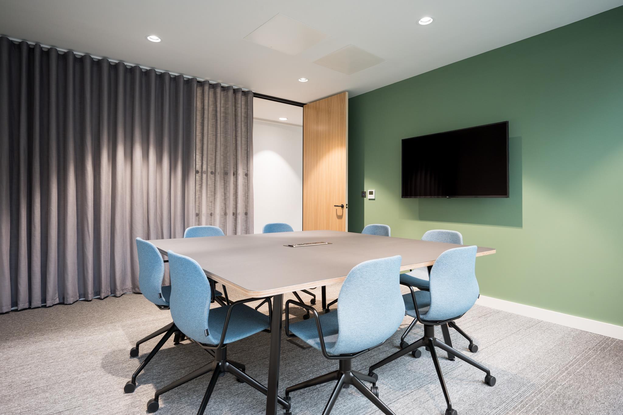 Meeting room at Platfform’s 70 New Oxford Street, styled with a green accent wall, soft blue chairs and a wall-mounted screen.