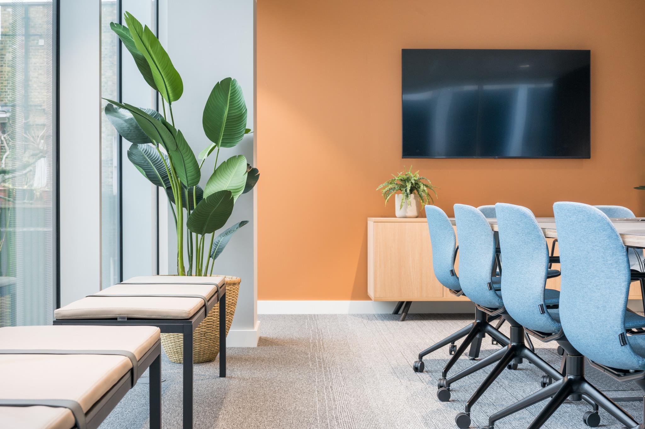 Detail view of the meeting room at Platfform’s 70 New Oxford Street, with soft blue chairs, an orange feature wall and lush greenery by the window.
