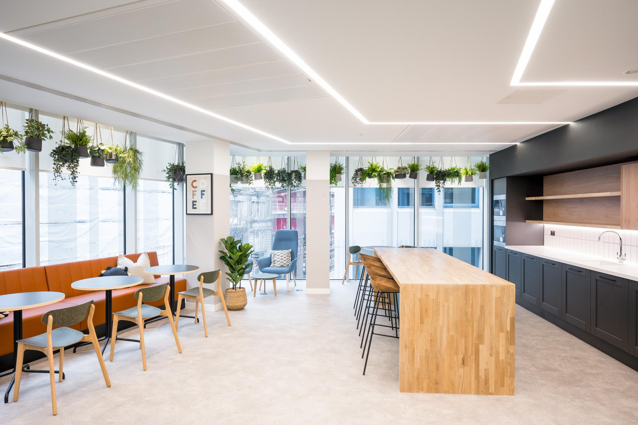 Bright teapoint at Platfform’s 70 New Oxford Street, featuring a timber island, banquette seating, and a full wall of greenery hanging in the windows.