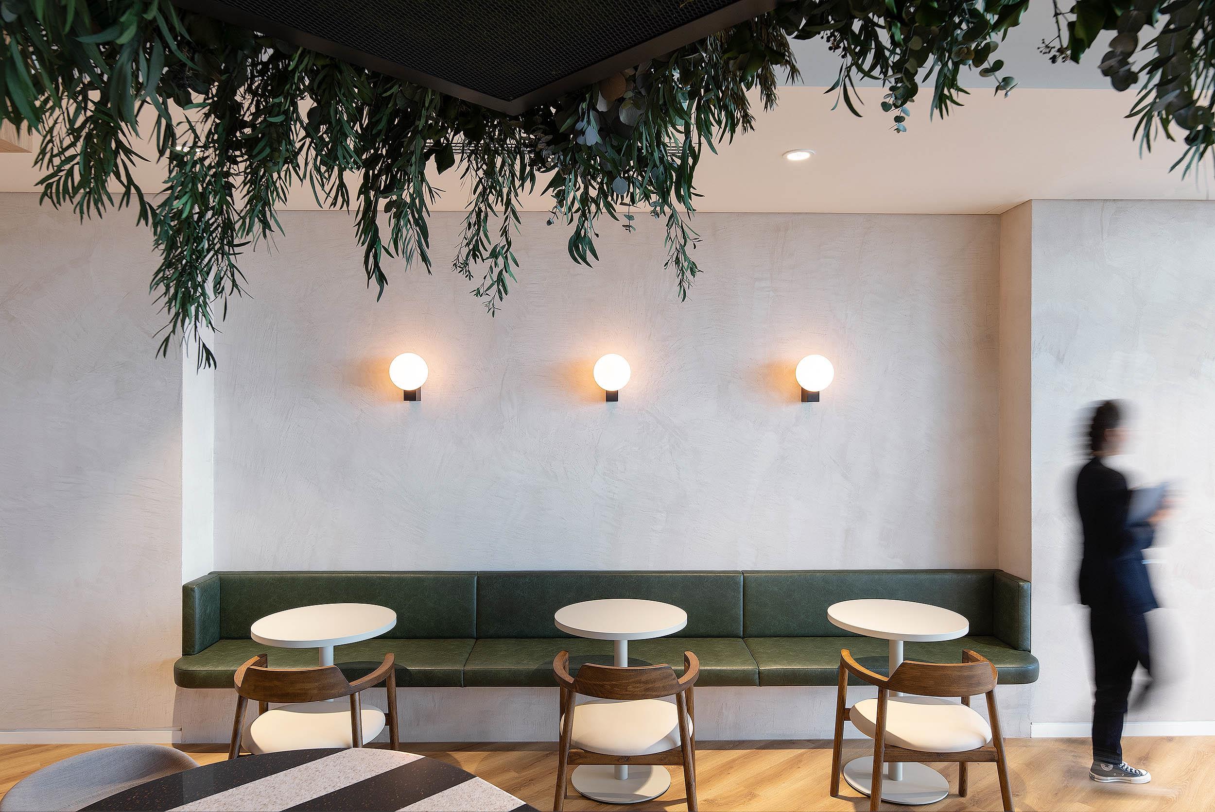 Built-in green leather banquette and soft timber chairs by Platfform for AMC, set beneath modern wall lights and greenery for a relaxed dining space.