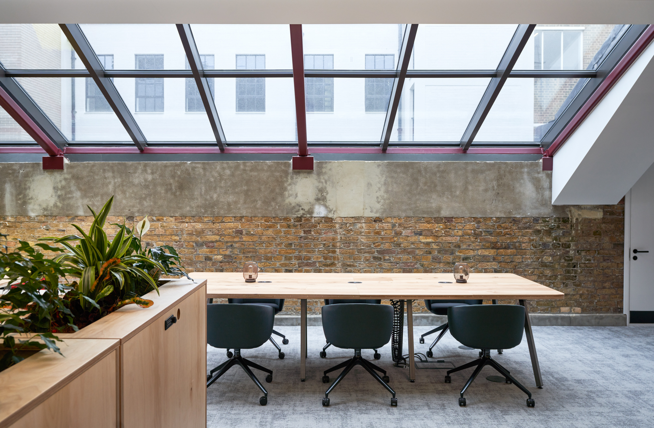 Natural light floods this workspace at Adyen, where Platfform supplied a minimalist desk setup beneath a striking sloped skylight and exposed brick backdrop.