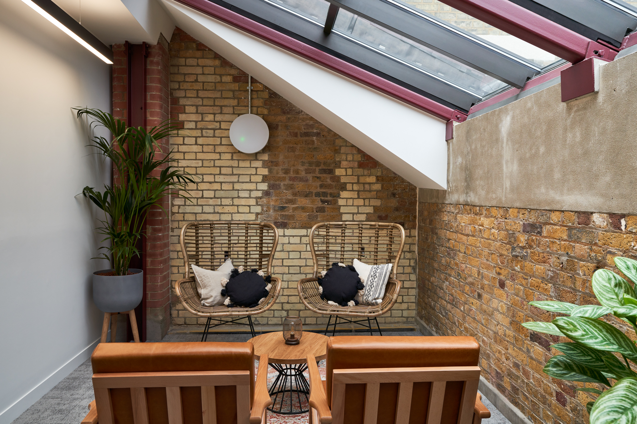 Breakout corner at Adyen with rattan lounge chairs and tan leather seating under a sloped skylight, styled with soft accents and greenery by Platfform.