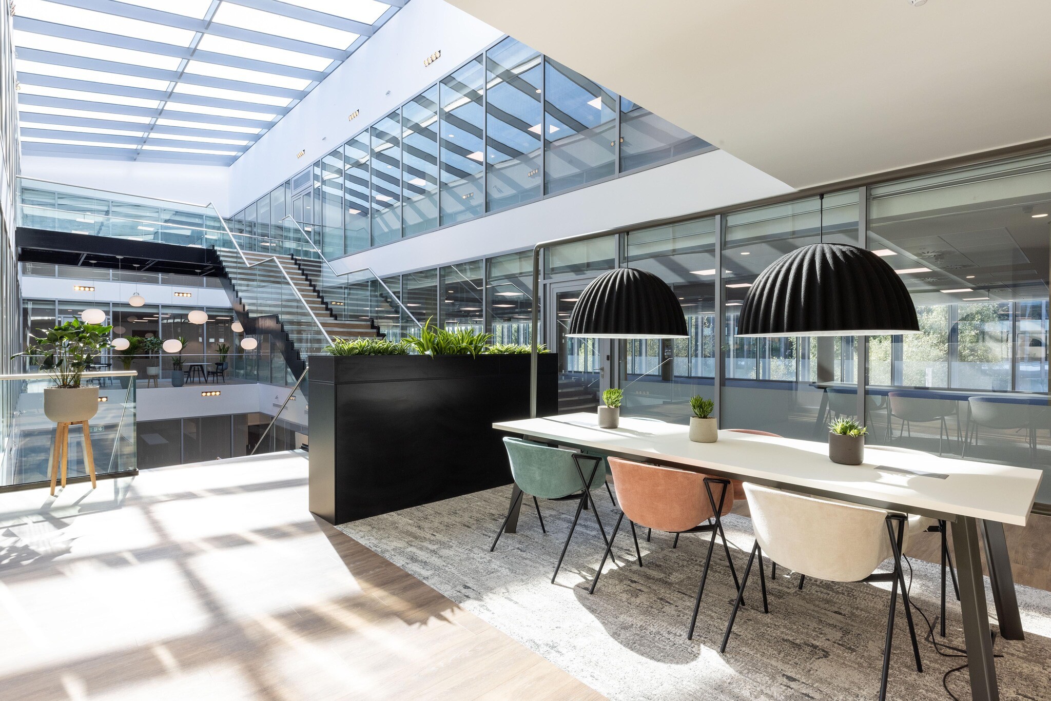 Breakout area at The Dock with soft-toned furniture by Platfform for Alchemy Asset Management, featuring a skylit atrium and textured black pendant lighting.
