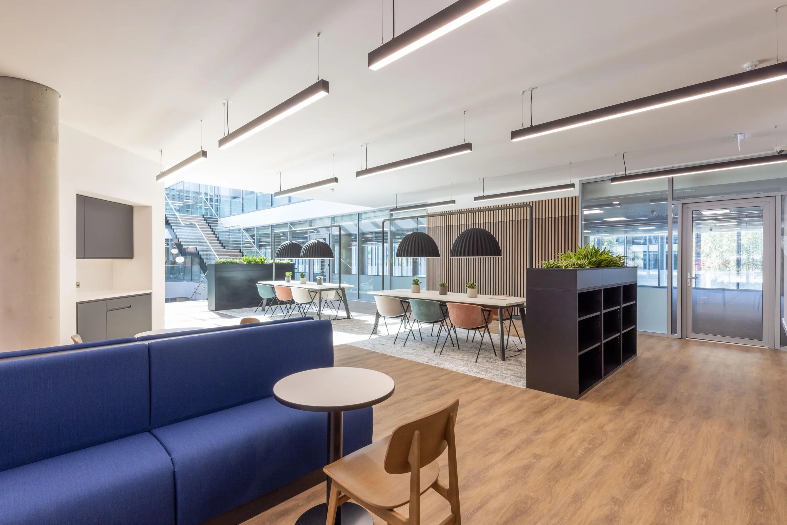 Flexible workspace at The Dock for Alchemy Asset Management, furnished by Platfform with colourful dining chairs, bold blue seating, and statement lighting under clean architectural lines.