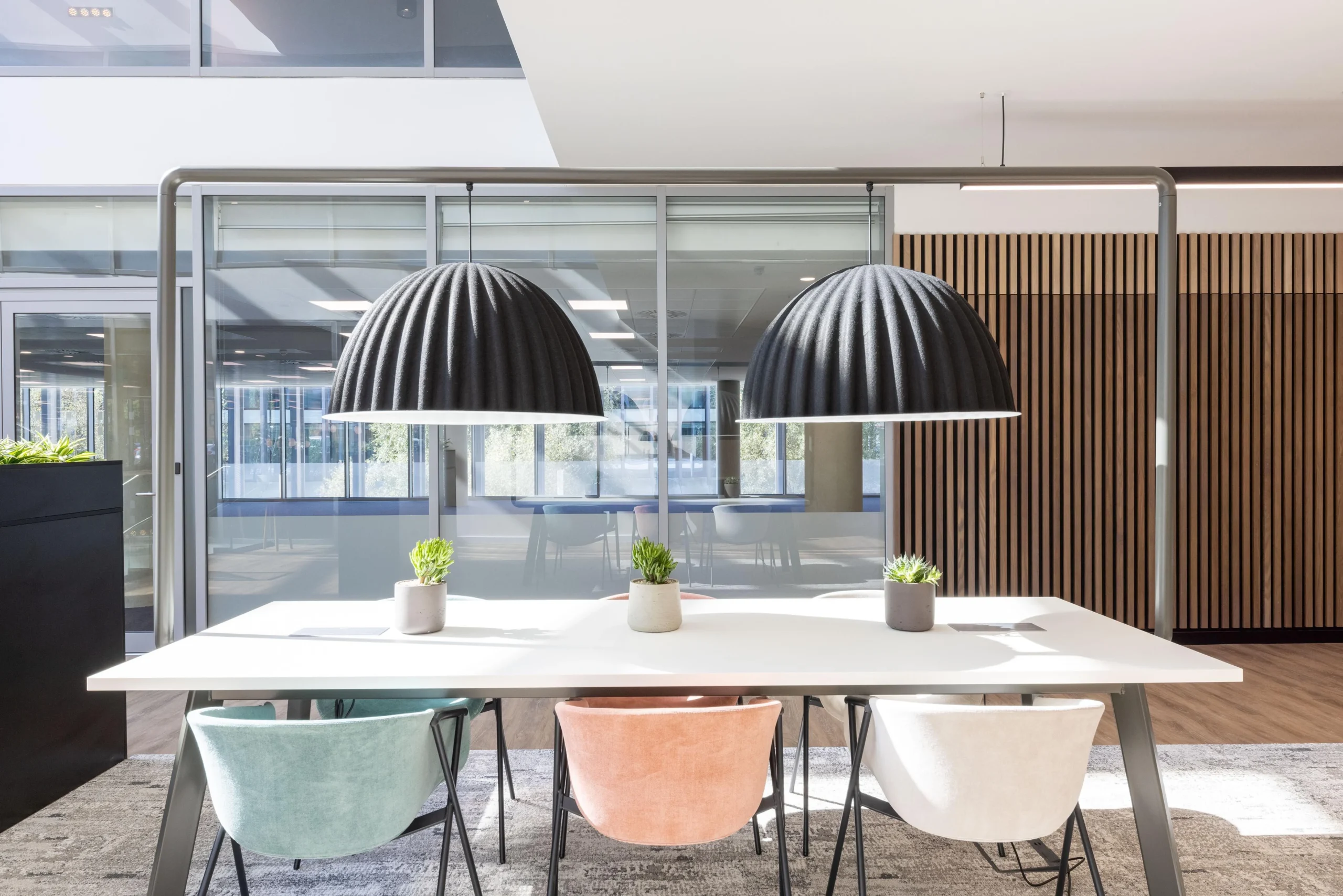 Close-up of a shared workspace at The Dock for Alchemy Asset Management, furnished by Platfform with pastel velvet chairs and oversized black pendant lights above a white desk.