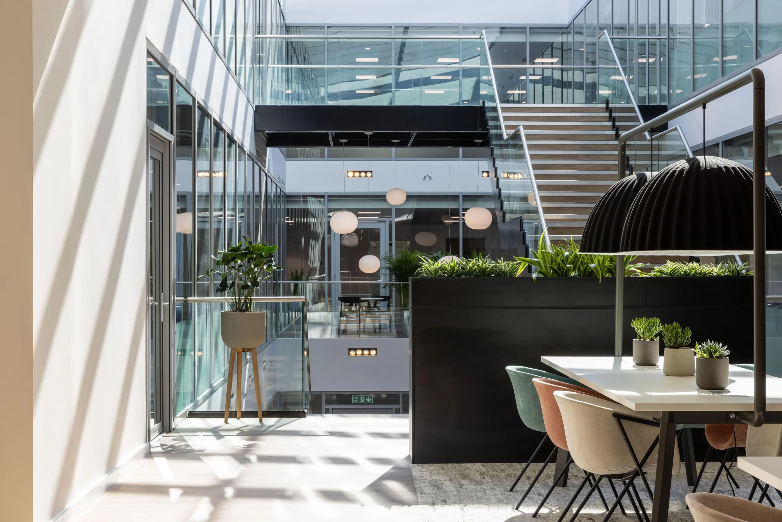 Atrium view at The Dock with soft pastel seating by Platfform for Alchemy Asset Management, framed by indoor planting, sculptural lighting, and a central staircase.
