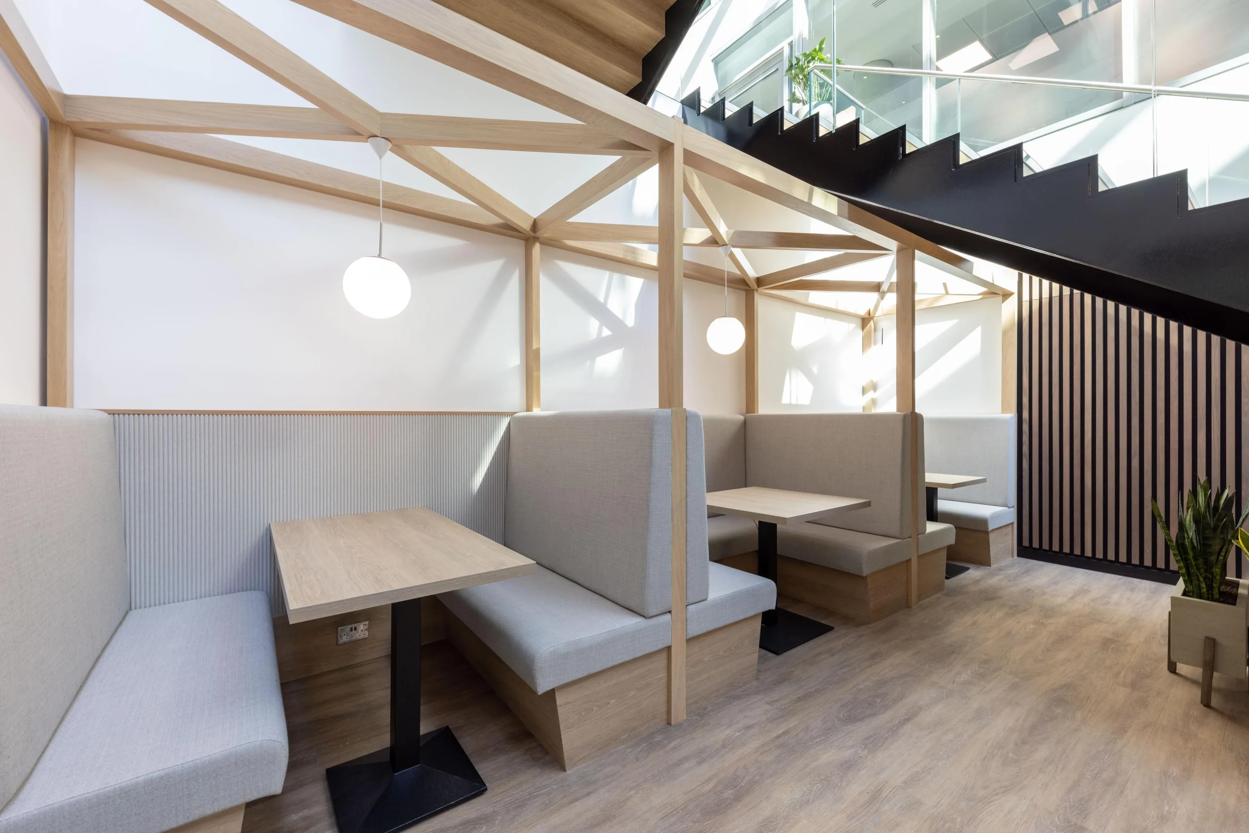 Bright communal space at The Dock for Alchemy Asset Management, furnished by Platfform with café-style tables, black chairs and potted greenery beneath a full-height atrium.