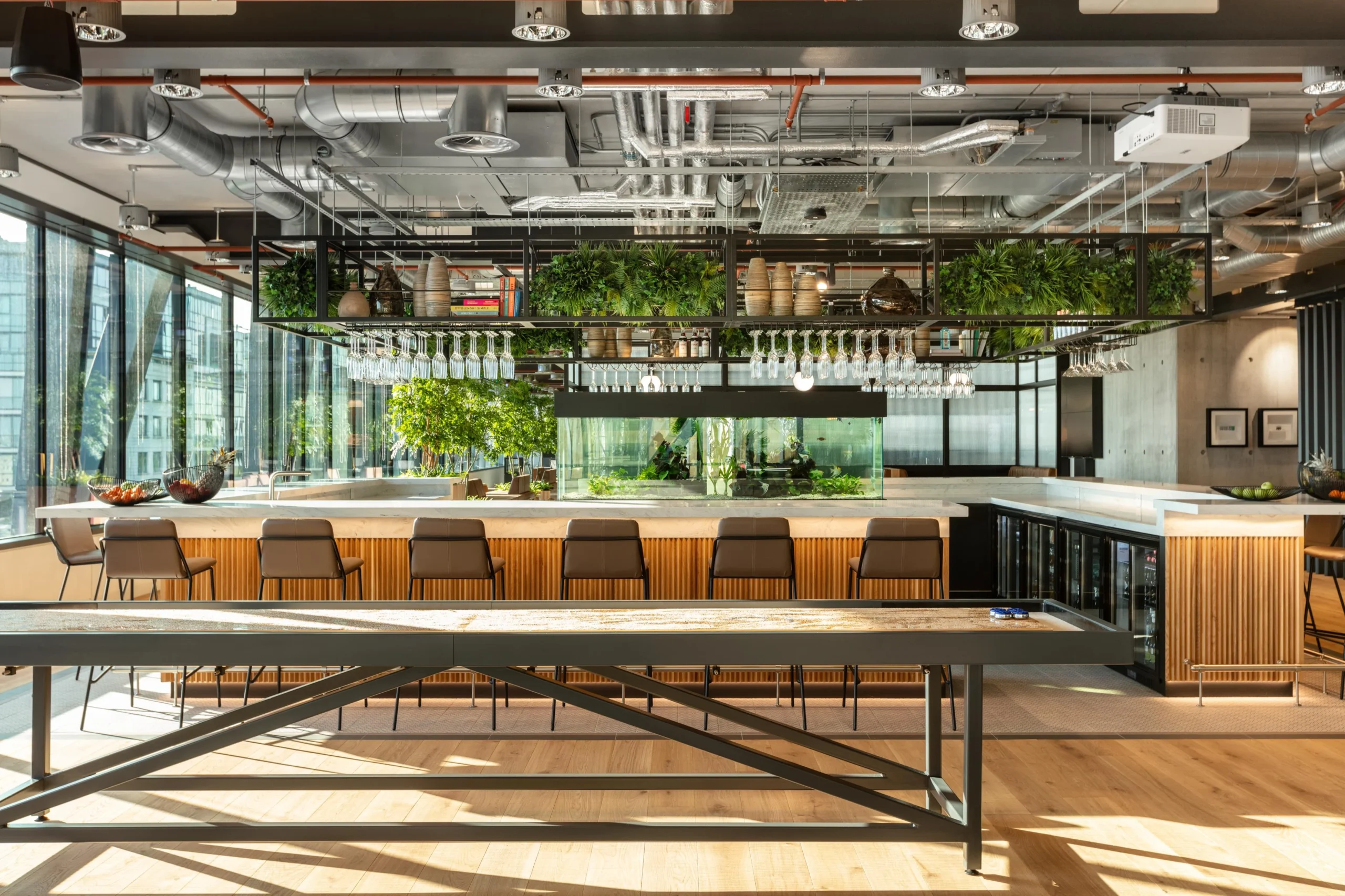 Lounge and bar area at Alpha FX designed with Platfform furniture, showcasing a central aquarium, overhead planting, and a long shuffleboard table for team downtime.