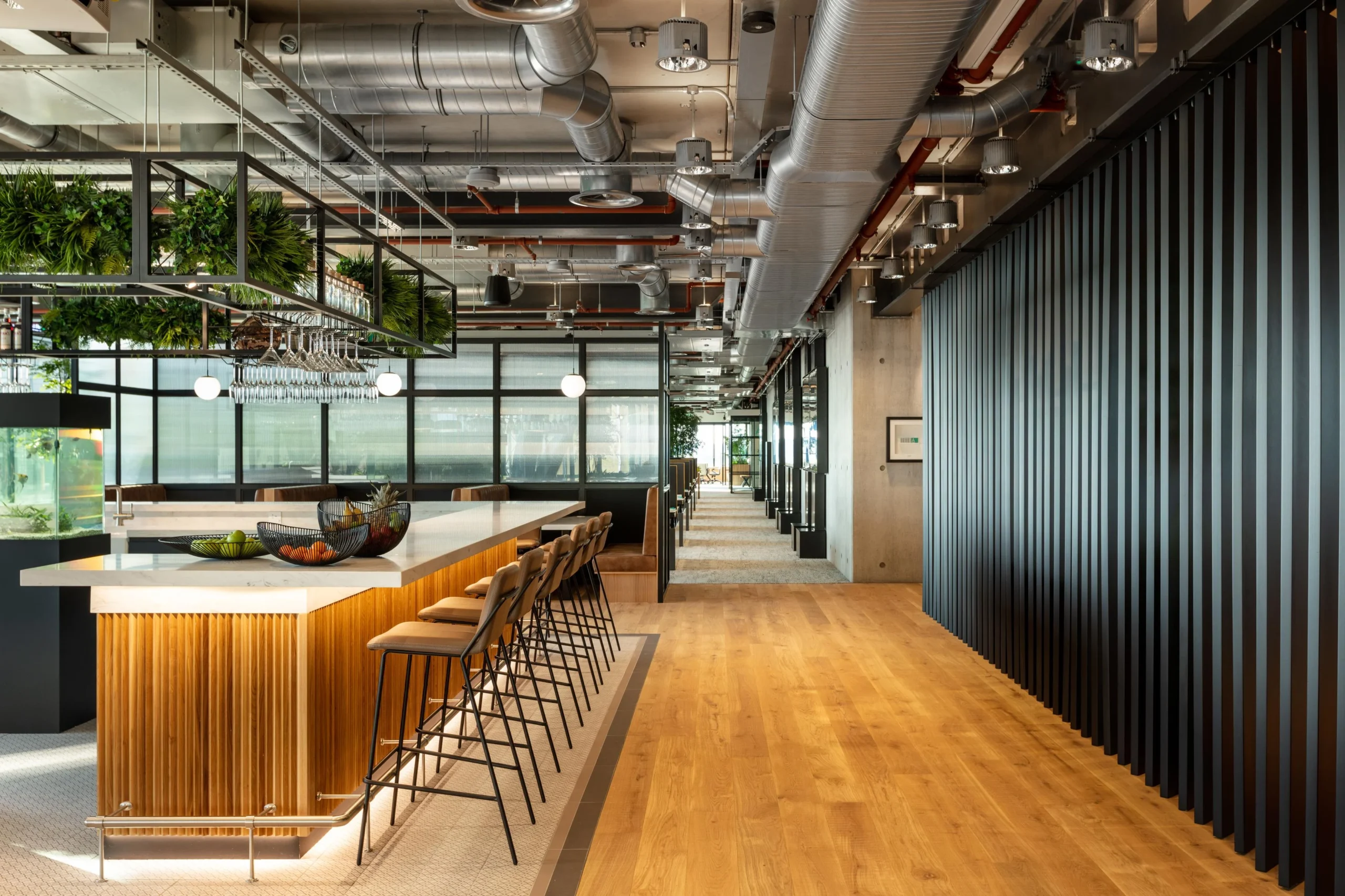 Teapoint area at Alpha FX featuring high stools and timber panelling, with Platfform-supplied furniture and integrated greenery enhancing the industrial office interior.