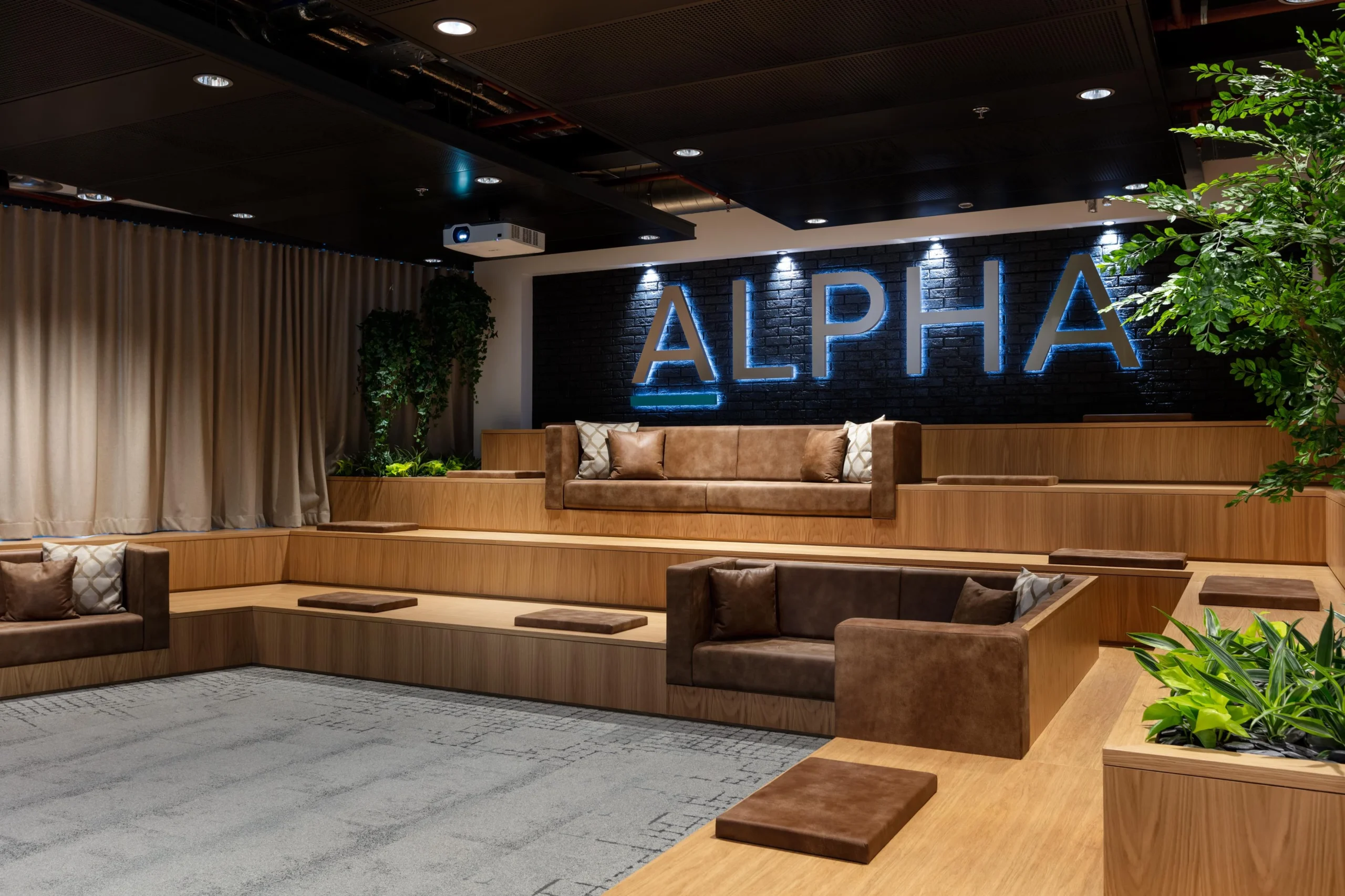 Tiered seating area at Alpha FX with integrated planters and bespoke soft furnishings by Platfform, set against a bold illuminated brand wall for events and presentations.