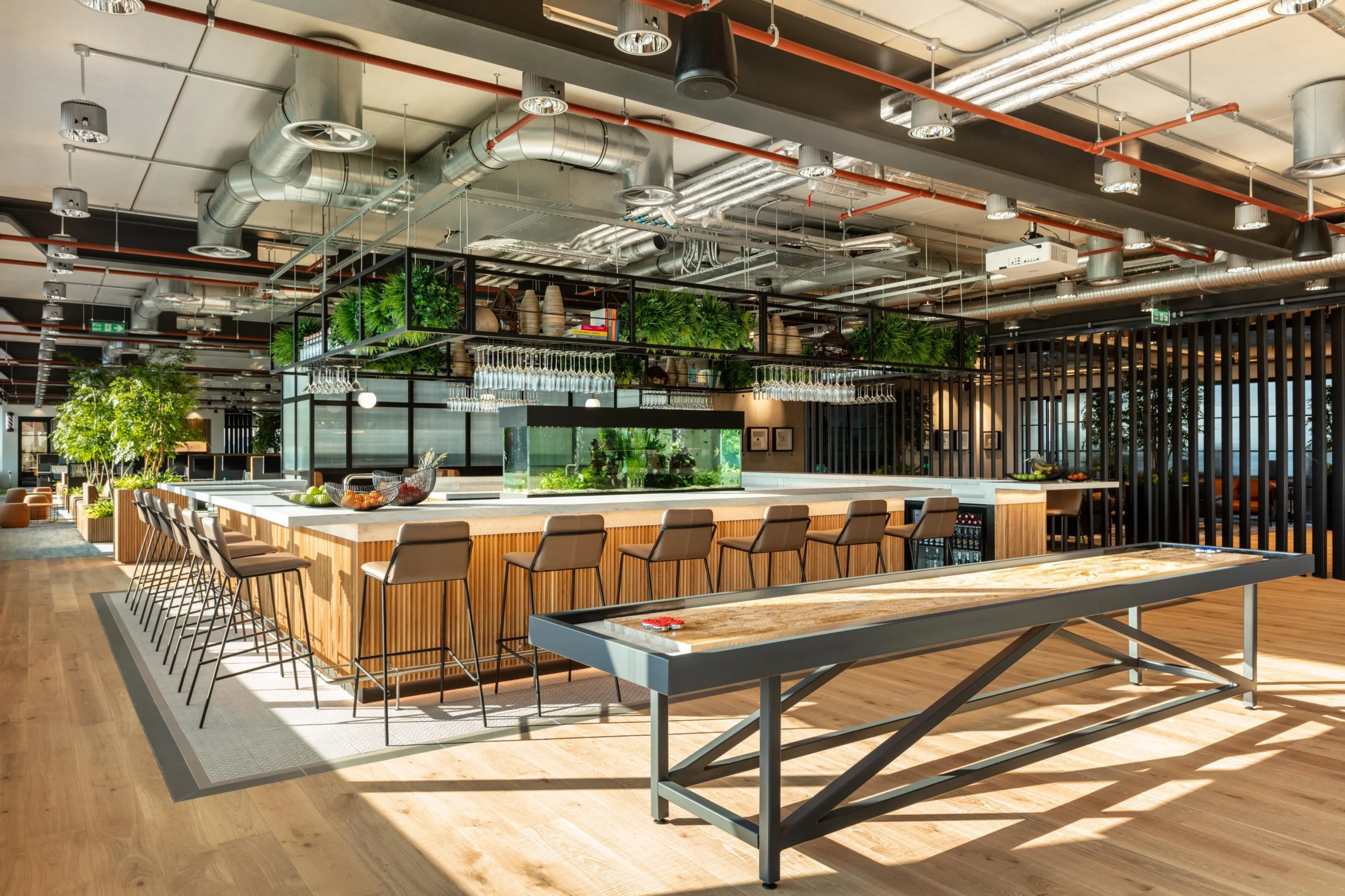 Vibrant social hub at Alpha FX with a central bar, aquarium, and shuffleboard table, furnished throughout by Platfform to support team interaction and wellbeing.