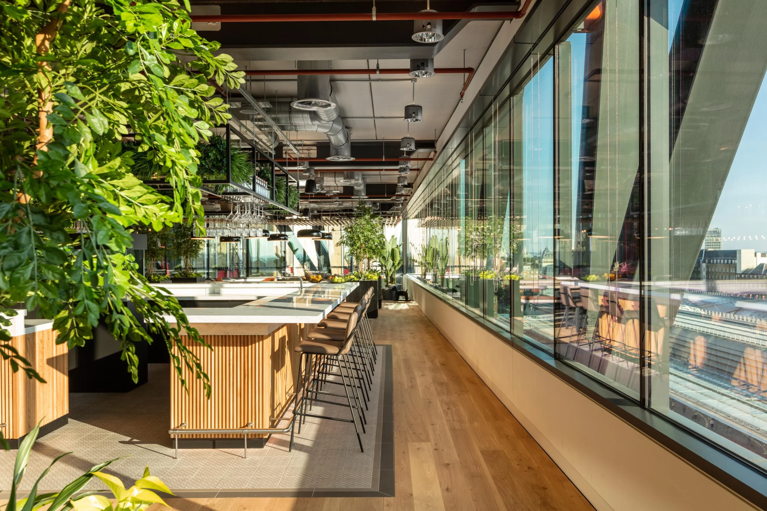 Light-filled bar and dining zone at Alpha FX with panoramic city views, bespoke stools and greenery-filled design by Platfform, blending hospitality and workspace.