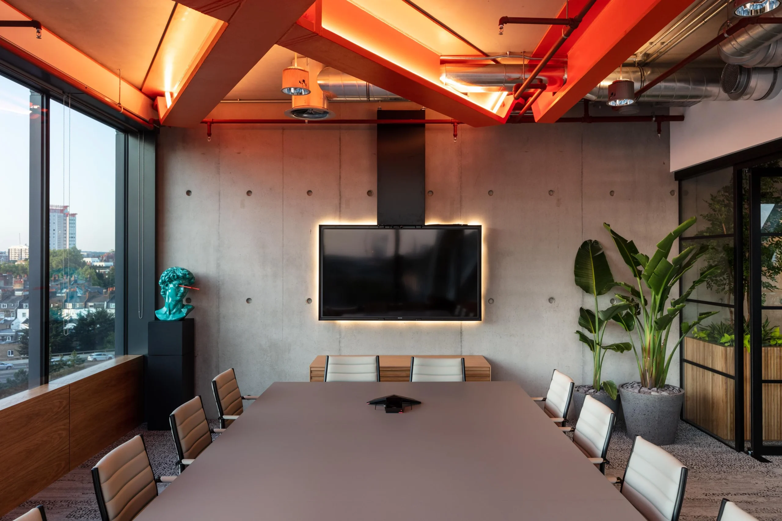 Alpha FX meeting room with a raw concrete wall, glowing screen, and clean-lined furniture by Platfform, framed by statement plants and sculptural details.