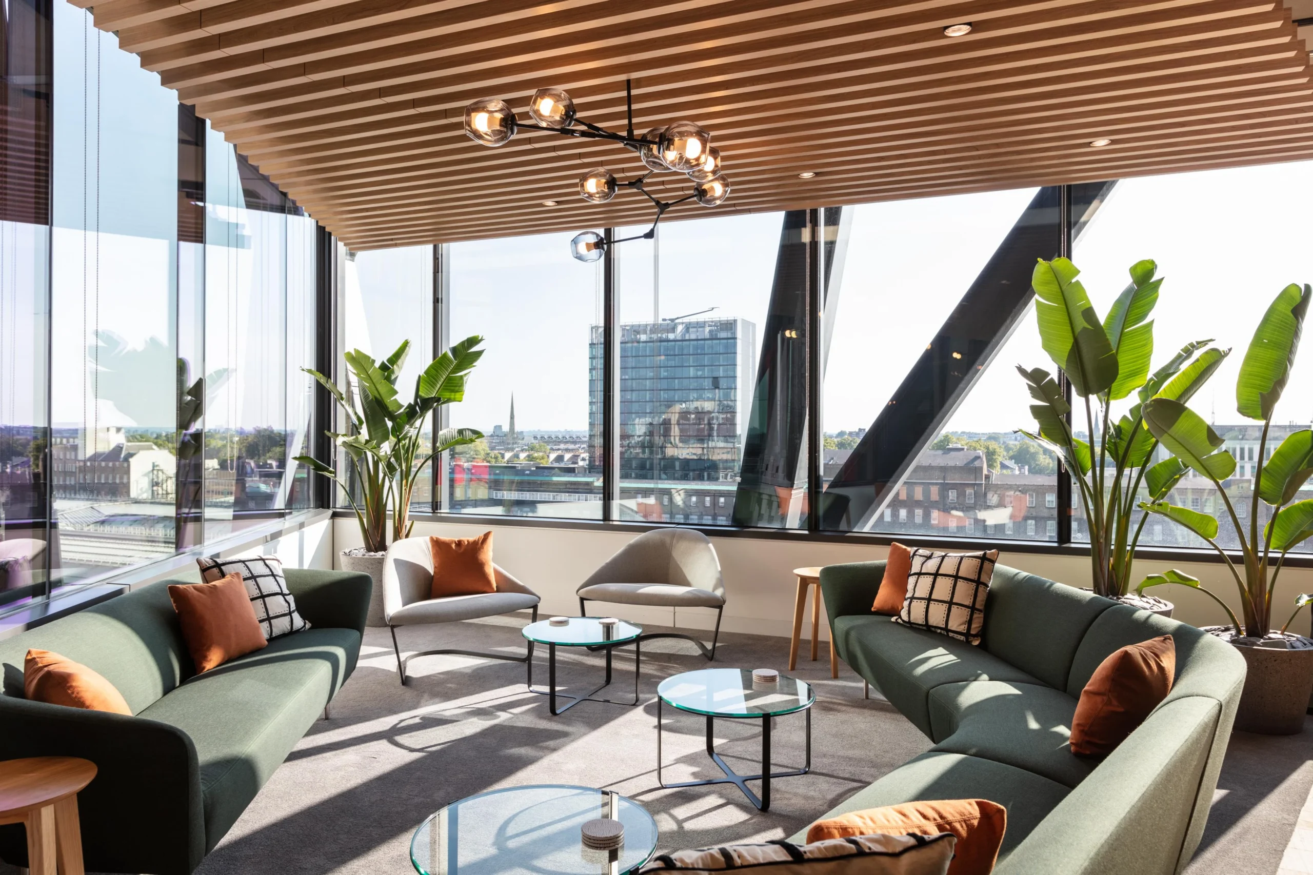 Corner lounge at Alpha FX with panoramic views, mid-century style sofas and chairs by Platfform, and layered greenery to soften the angular architecture.