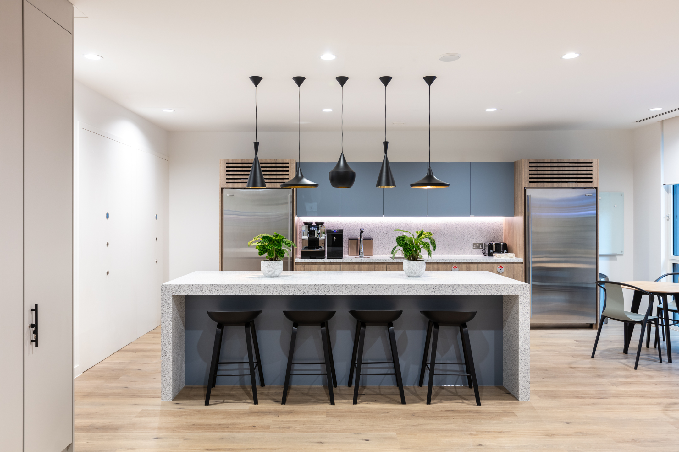 Teapoint area for an Asset Management Firm, fitted out with modern furnishings by Platfform, featuring a terrazzo island, black stools, and pendant lighting.