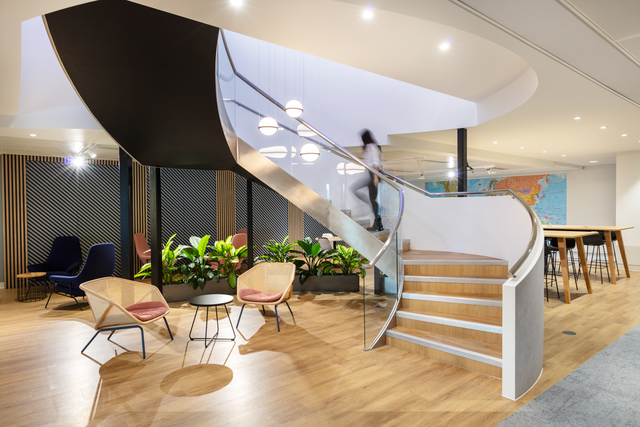 Curved staircase at Baringa surrounded by biophilic planting, modern seating, and a collaborative work area with a world map feature wall.