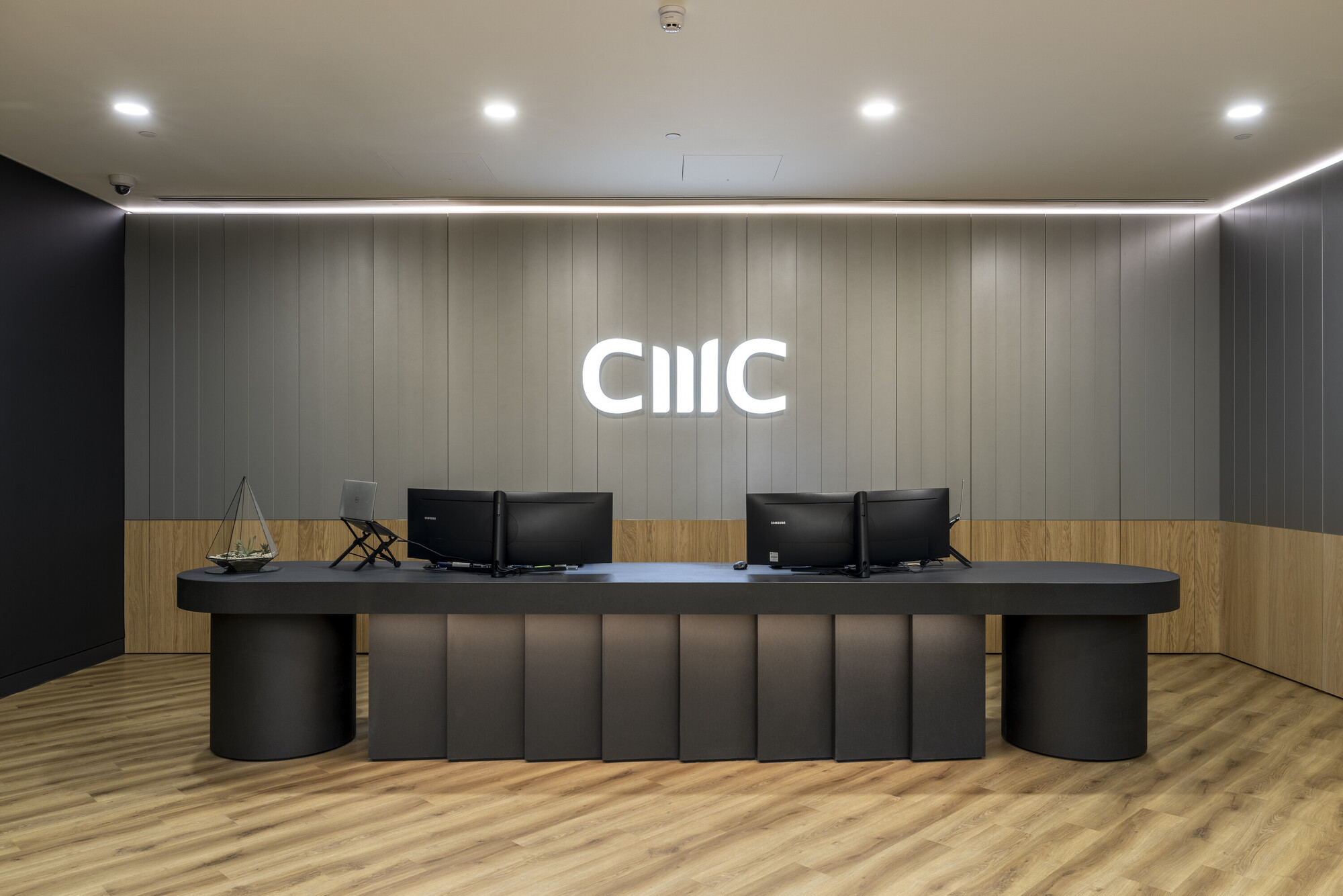 The sleek reception desk at CMC Markets' London HQ, designed by Platfform, features wood panelling, integrated lighting, and modern finishes.