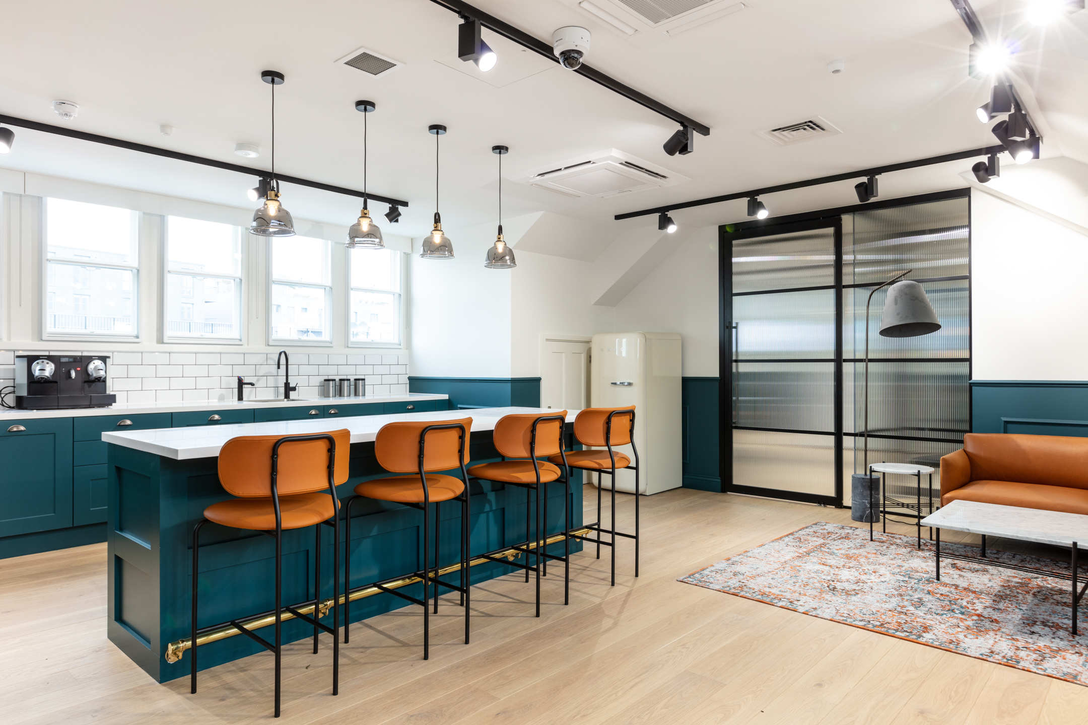 Teapoint and breakout area for Cain International, with bespoke furniture specified by Platfform including tan bar stools, a teal island unit and a mid-century inspired lounge set.