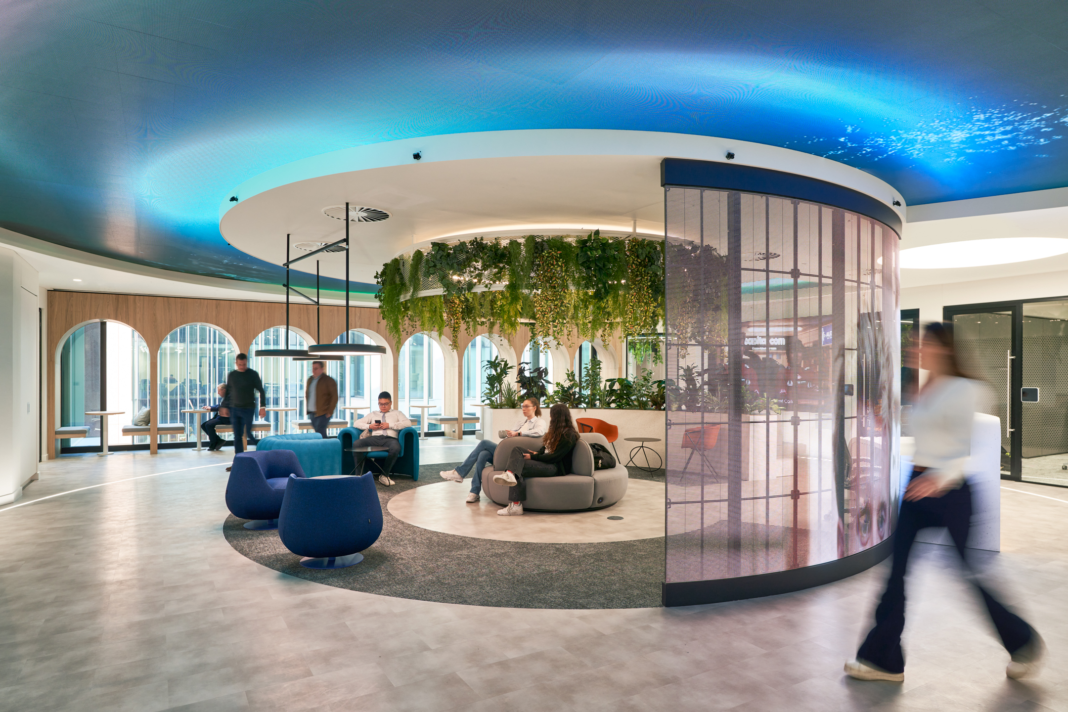Reception and breakout space at capital.com office with biophilic ceiling feature, curved mesh wall and relaxed lounge seating.