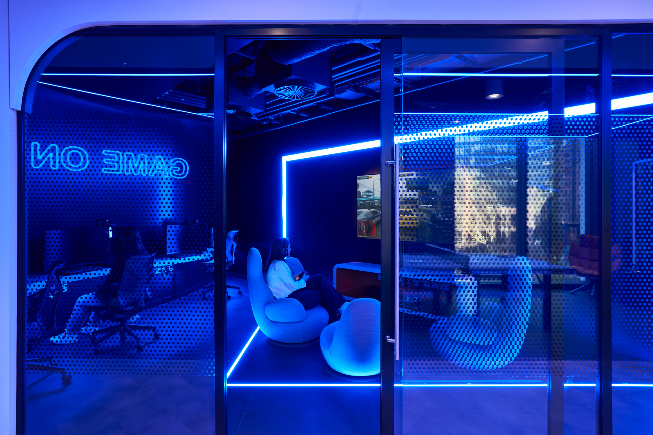 Gaming room at capital.com office with neon lighting, ergonomic chairs and high-spec consoles visible through perforated glazing.