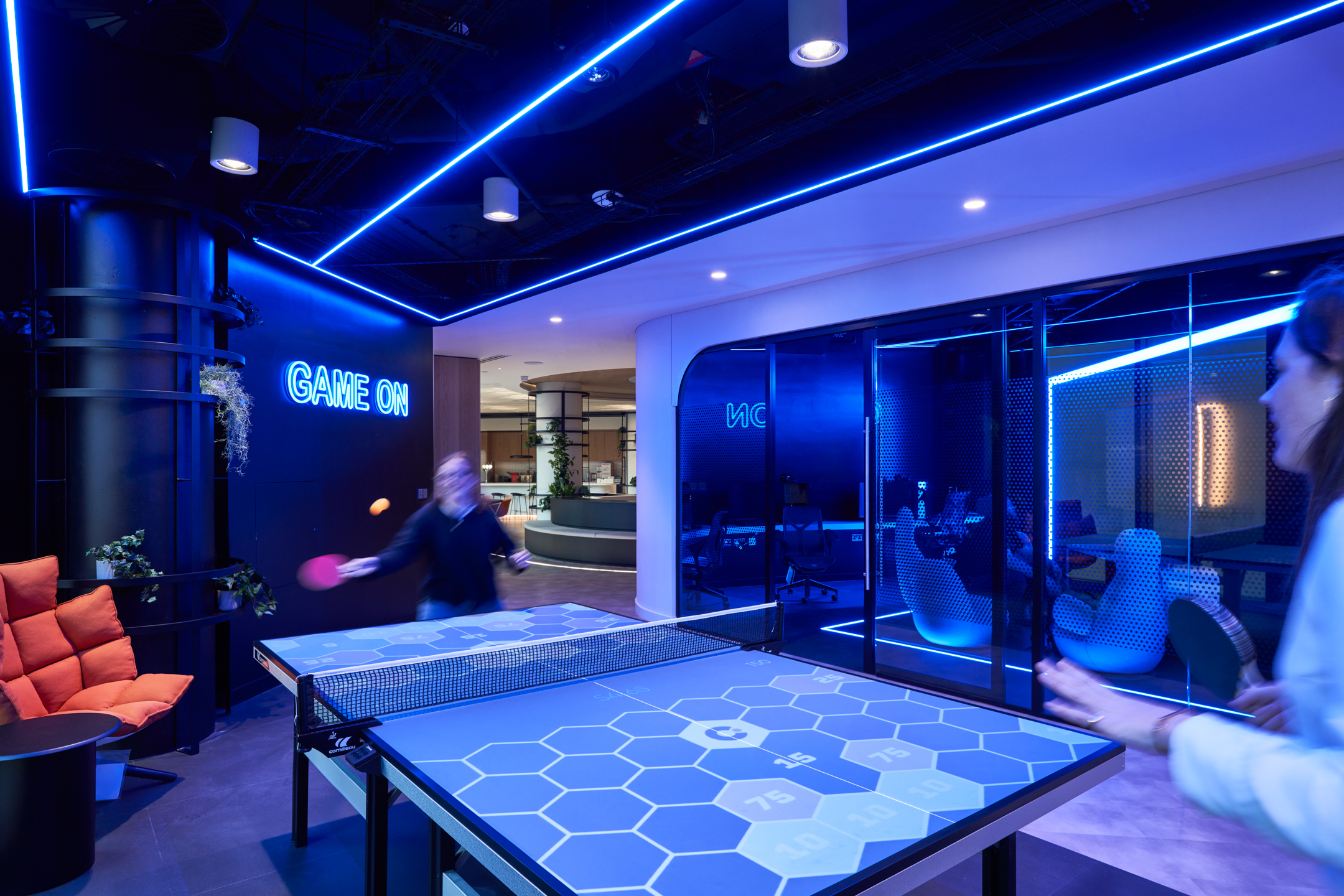 Interactive ping pong area at capital.com office with neon 'Game On' sign, digital scoring table and breakout lounge seating.