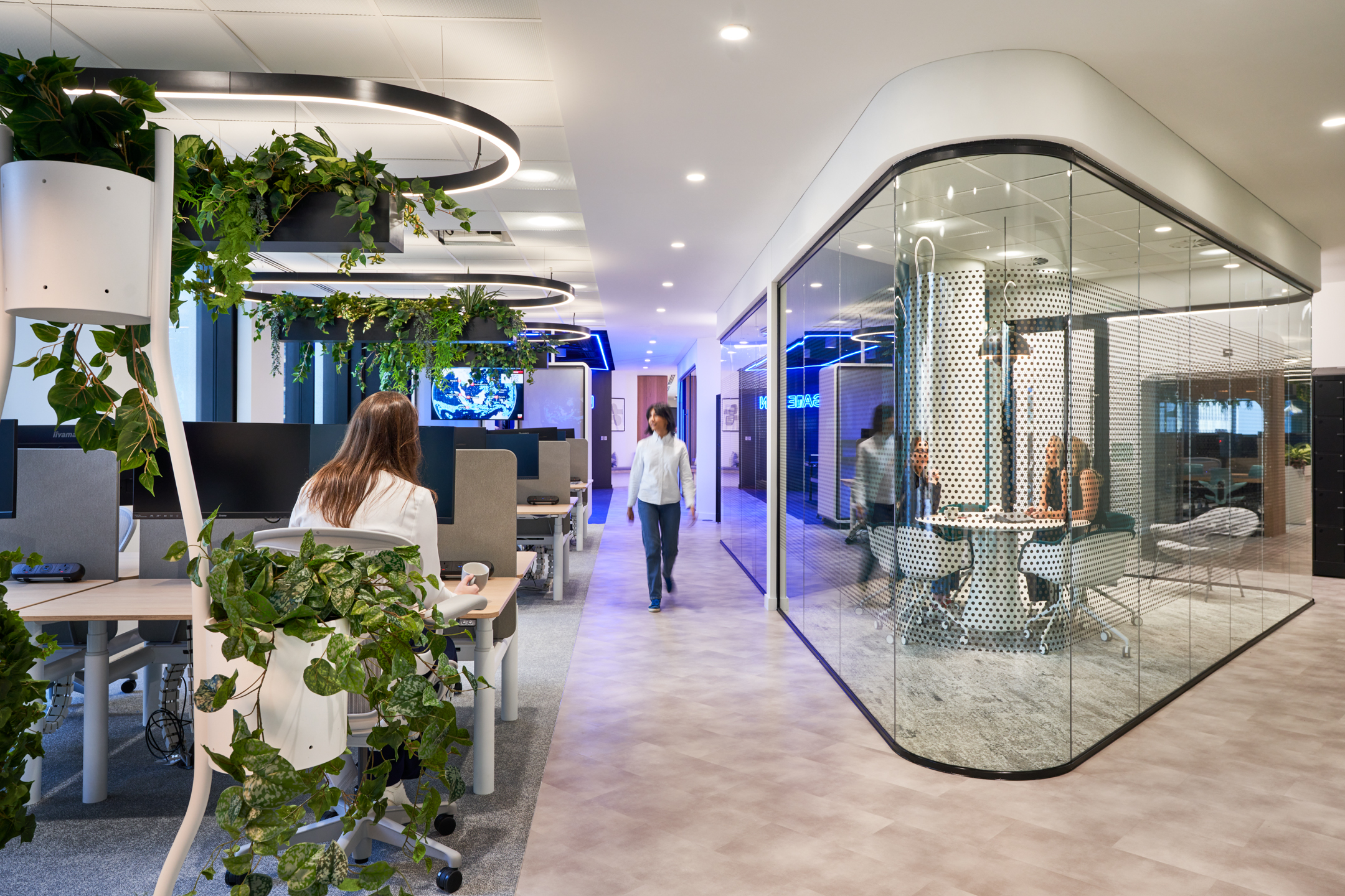 Workspace at capital.com featuring height-adjustable desks, biophilic lighting and a glazed meeting pod with perforated detail.