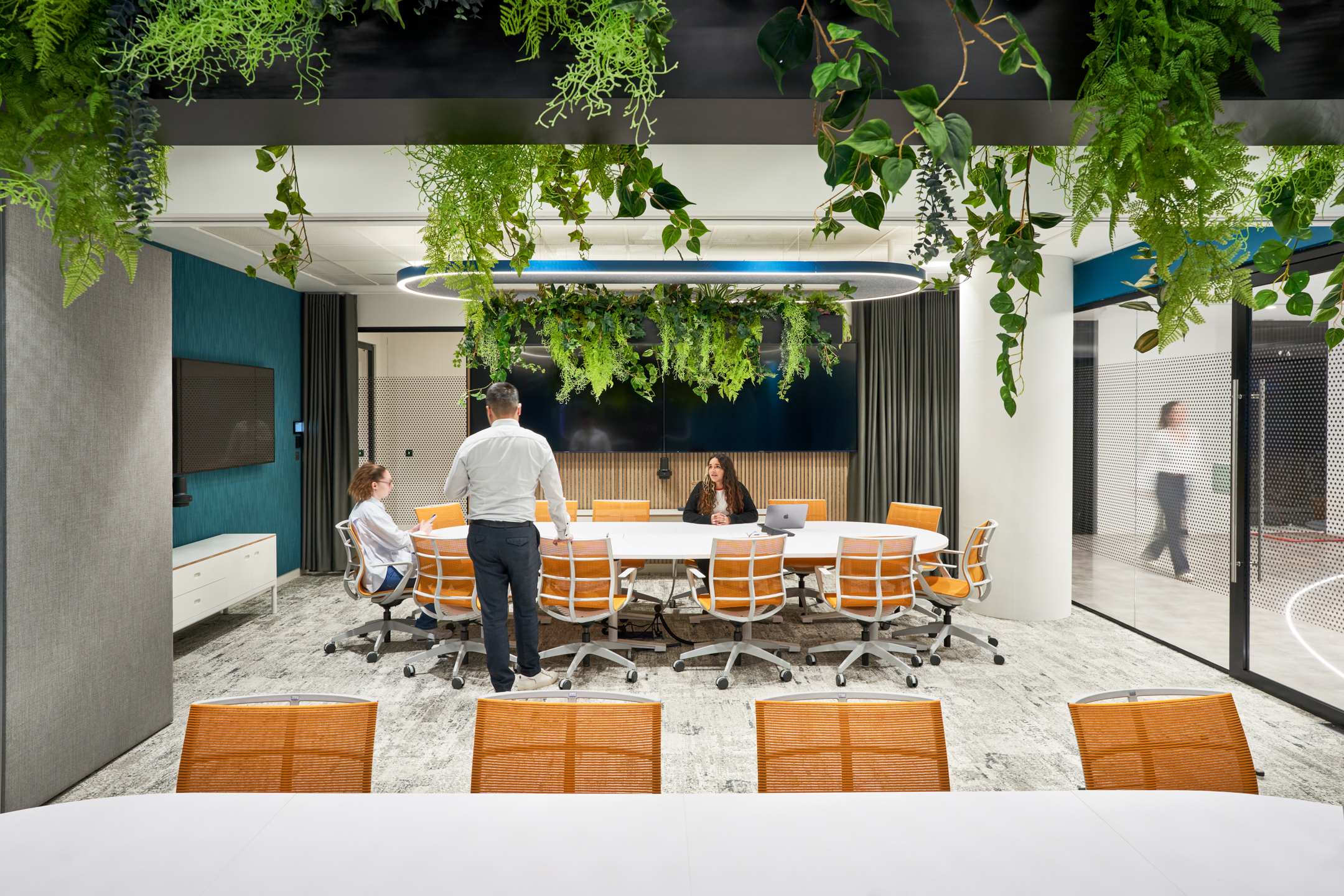 Capital.com boardroom fitted with a custom white meeting table and orange mesh-back chairs supplied by Platfform, set beneath a statement biophilic lighting feature.