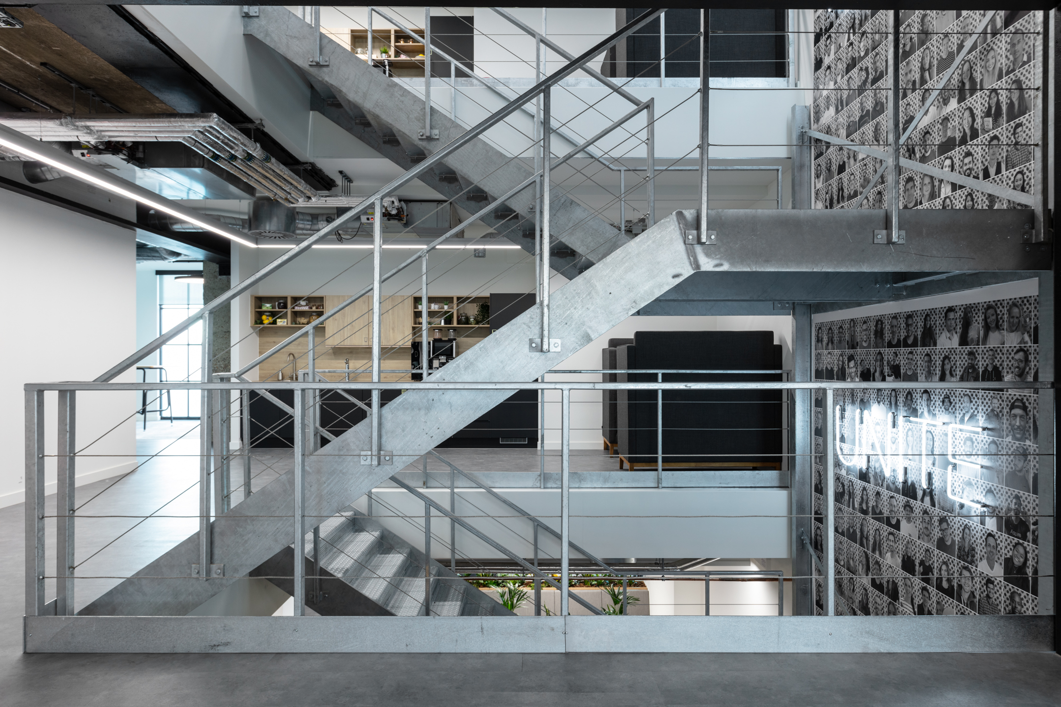 Open stairwell at Checkout.com featuring raw metal finishes, monochrome portraits and a glowing 'Unite' neon sign on the wall.