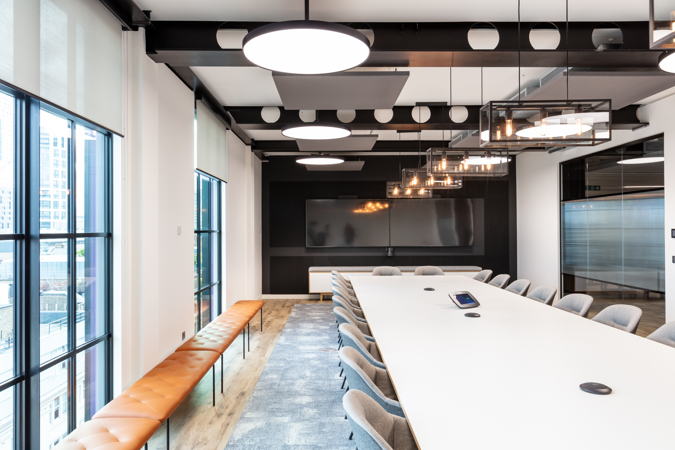 Meeting room at Checkout.com with a long white meeting table, pendant lighting and full-height windows overlooking the city.