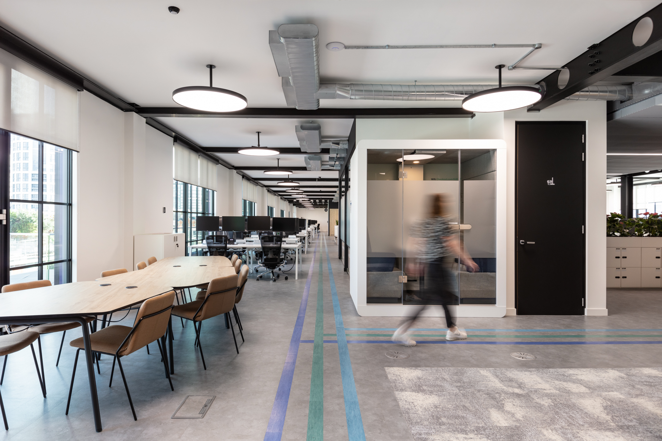Open-plan workspace at Checkout.com with modern desking, acoustic meeting pods, and colourful wayfinding lines across the floor.