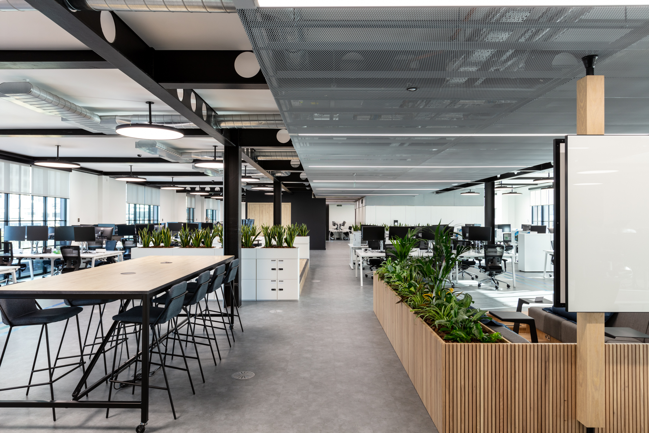 Modern office interior at Checkout.com with bar-height collaboration tables, open-plan desking, and planting used to define zones.