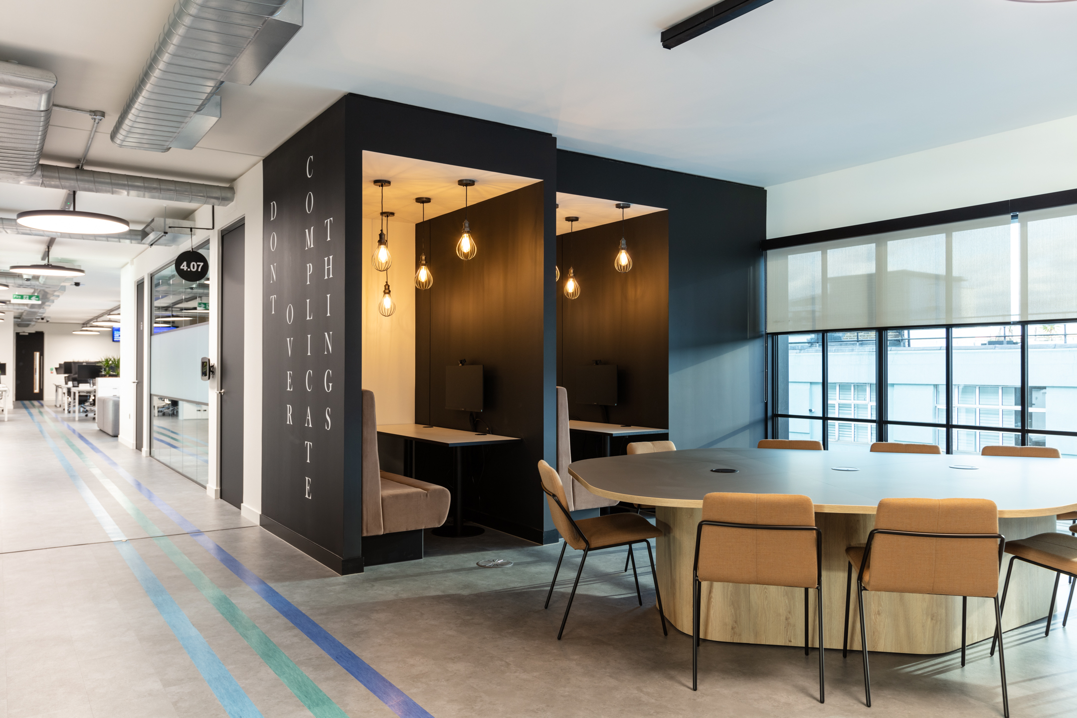 Focus pods and round collaboration table at Checkout.com, with ambient lighting and the phrase ‘Don’t overcomplicate things’ on the wall.