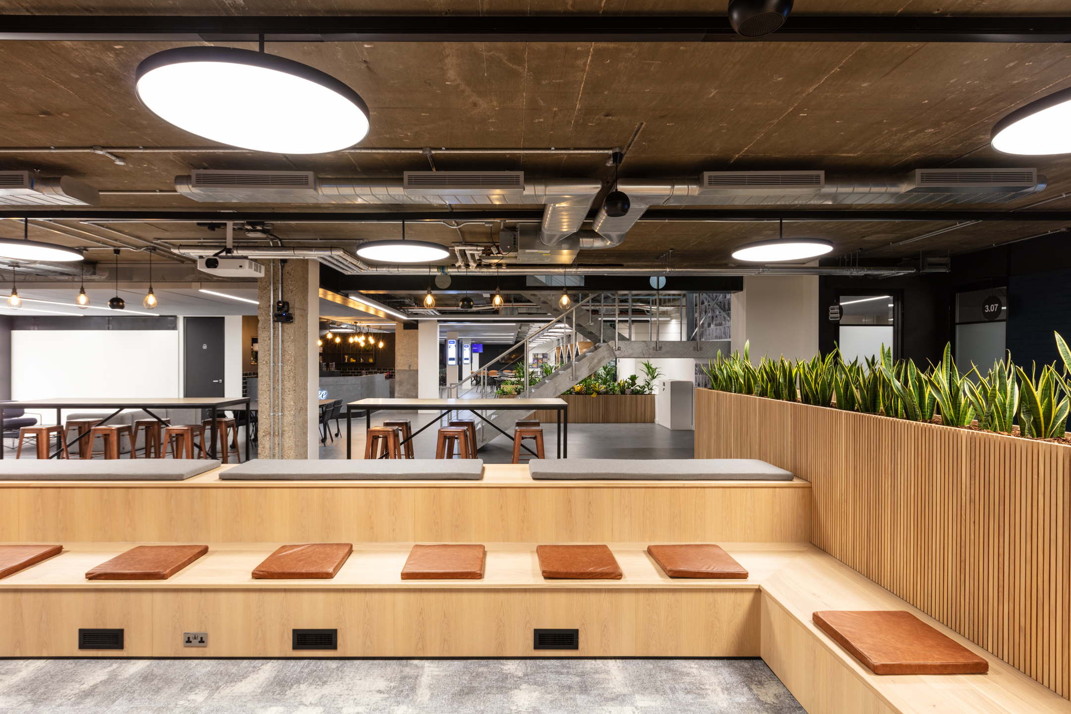 Tiered seating area at Checkout.com with leather cushions, built-in power, integrated planters and views into the social and stairwell zones.