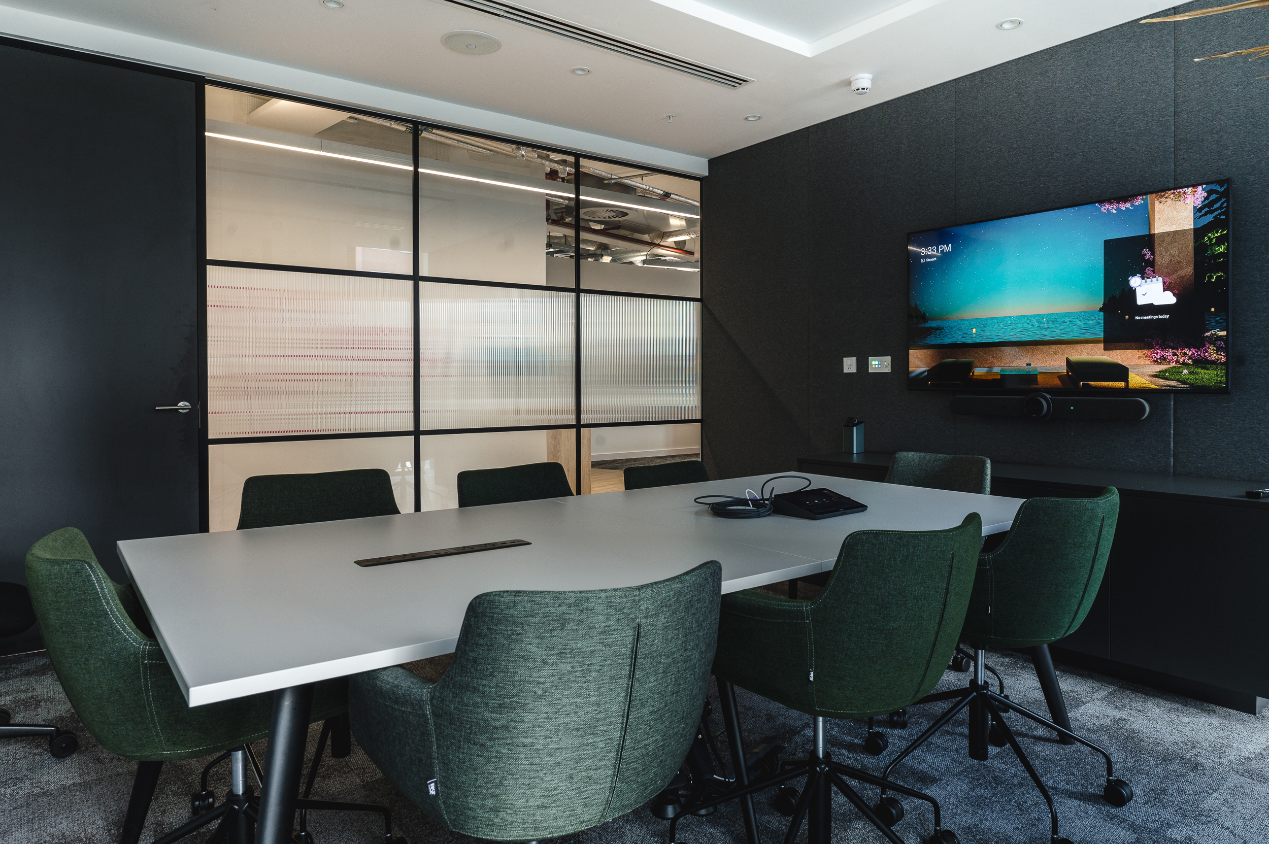 Meeting room at Everyone TV with a sleek white table and green upholstered task chairs.
