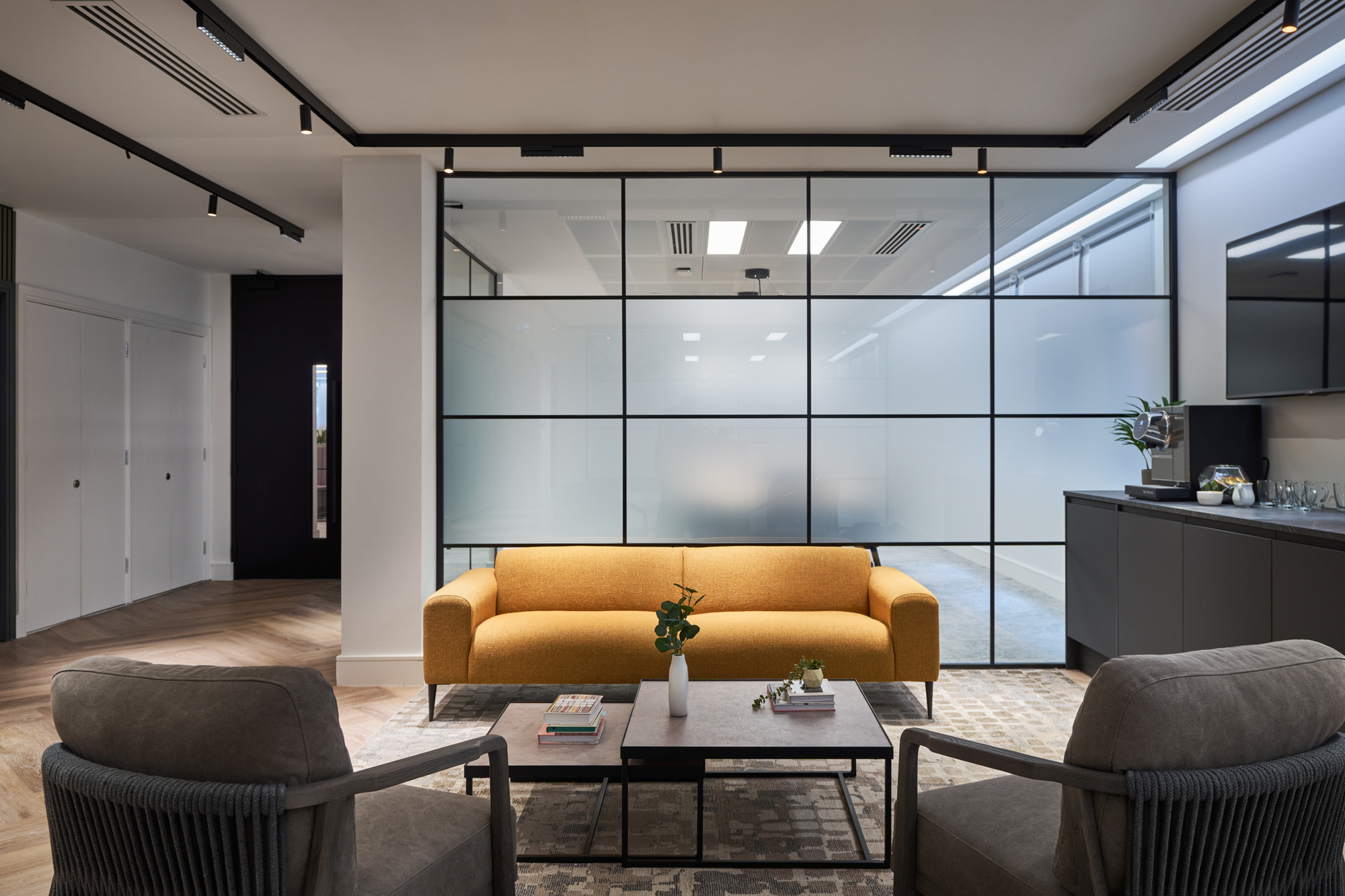 Gemserv's lounge area designed by Platfform, featuring a mustard sofa, grey armchairs, and frosted glazing for a modern yet inviting atmosphere.