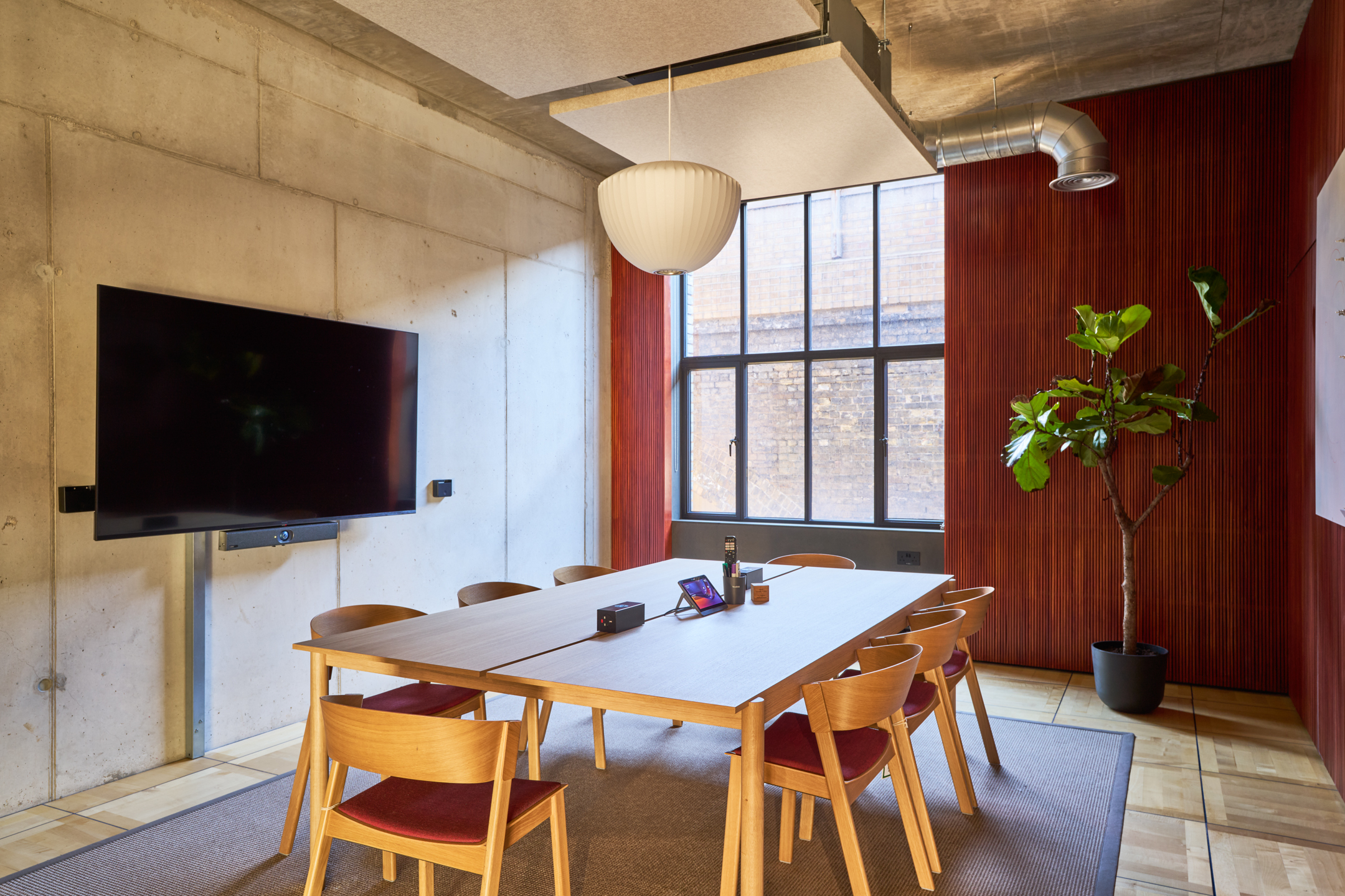Intimate meeting space featuring minimalist wooden furniture, red accents, and vibrant greenery.
