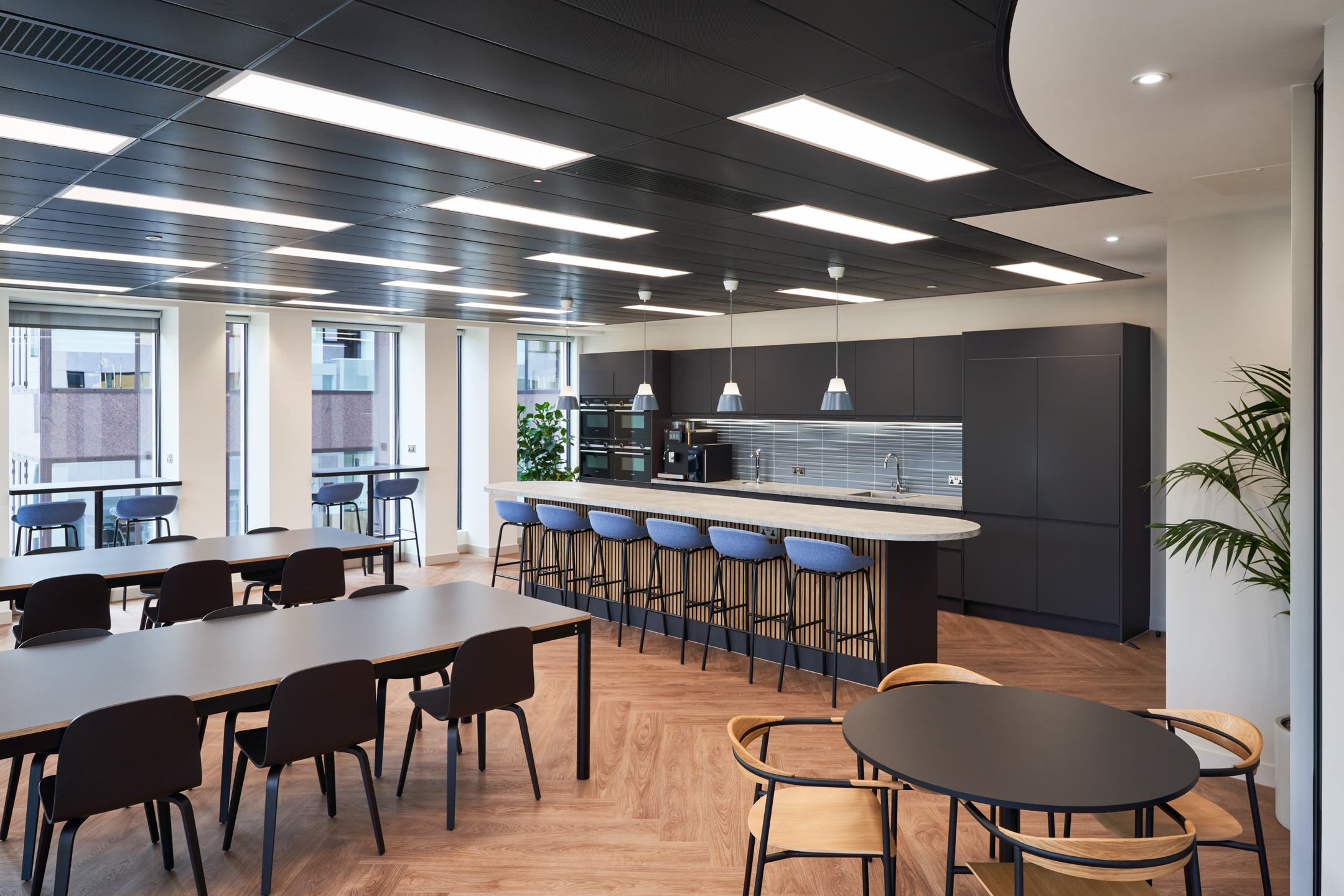 Contemporary office kitchen at KPI Ocean Connect, with black cabinets, a marble countertop, and pendant lighting, designed by Platfform for a stylish workspace.