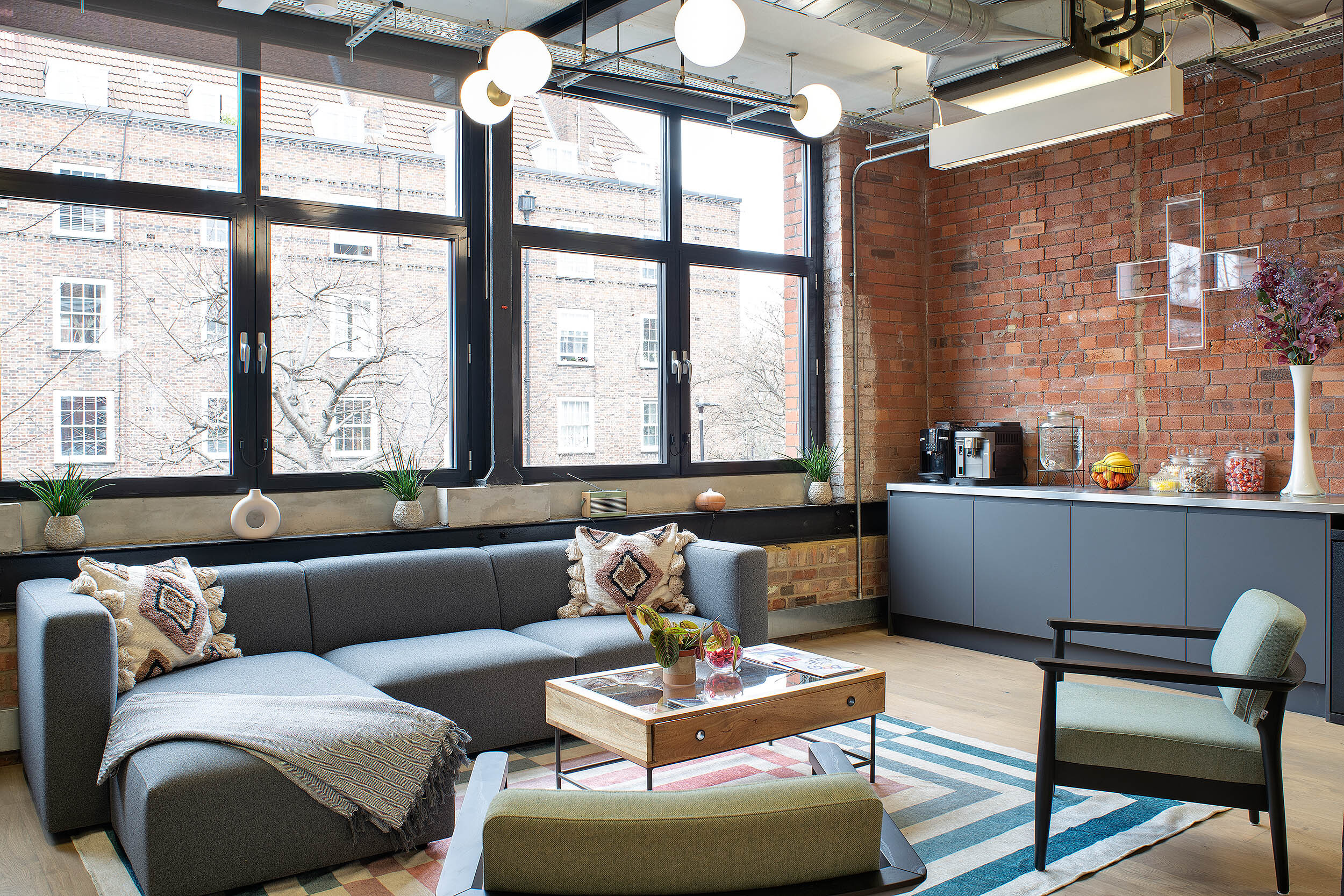 Cosy breakout area at the Kin & Carta office designed by Platfform, featuring a modern sofa, exposed brick walls, and a teapoint with coffee facilities.