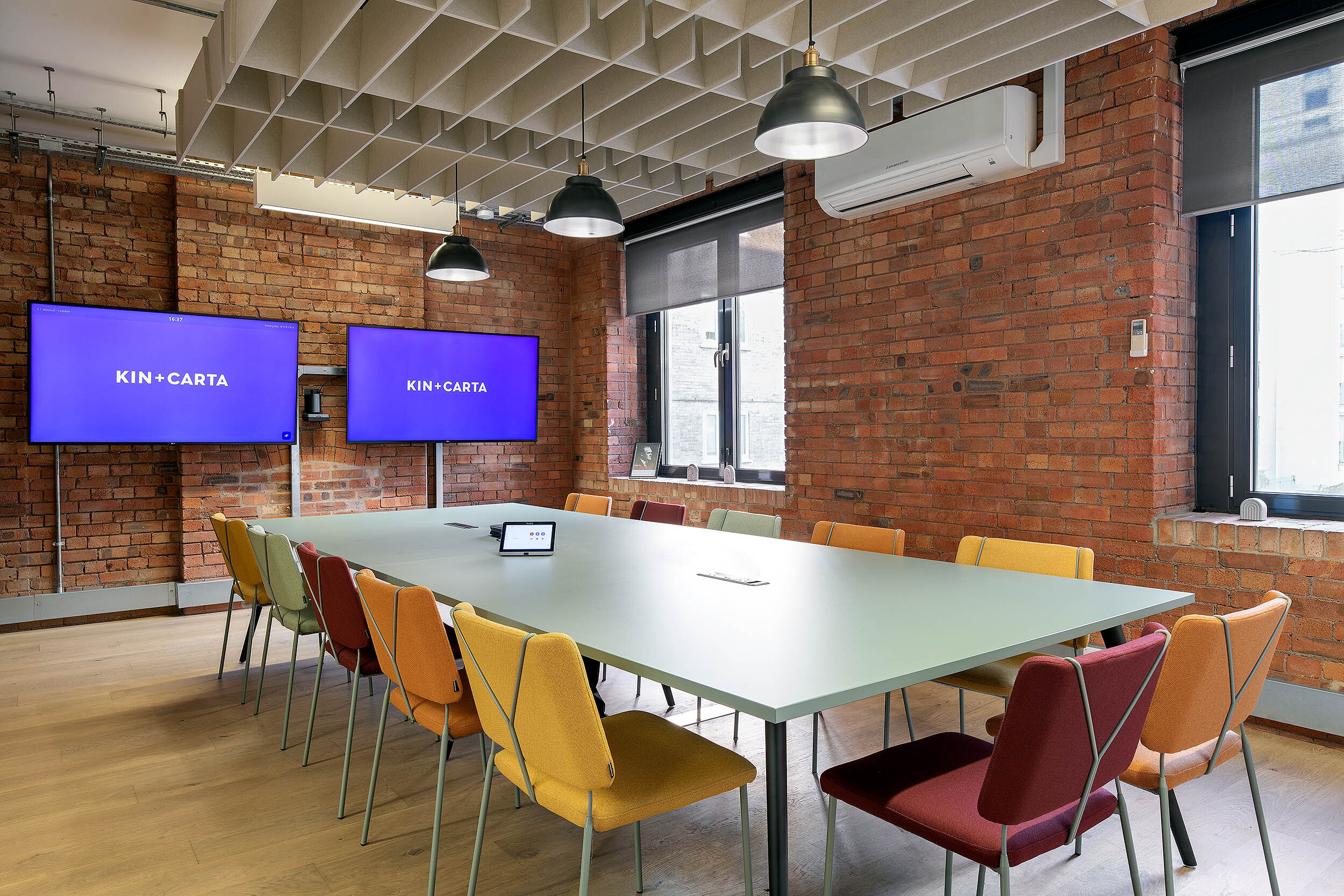 Modern meeting room at the Kin & Carta office, furniture by Platfform, with colourful chairs, a central table, and dual screens for presentations.